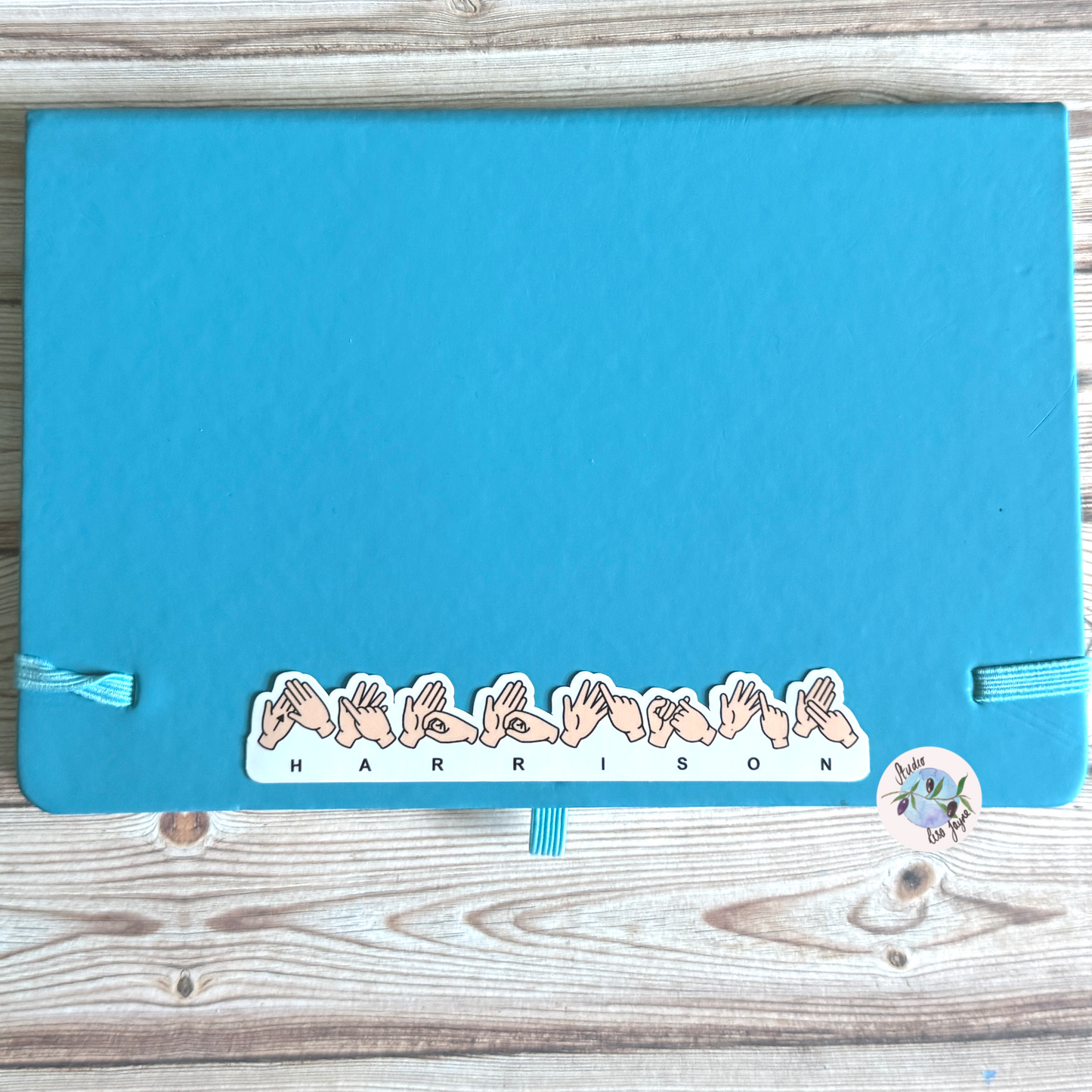 Blue notebook with decorative sticker with name 'Harrison' spelt using BSL British Sign Language
