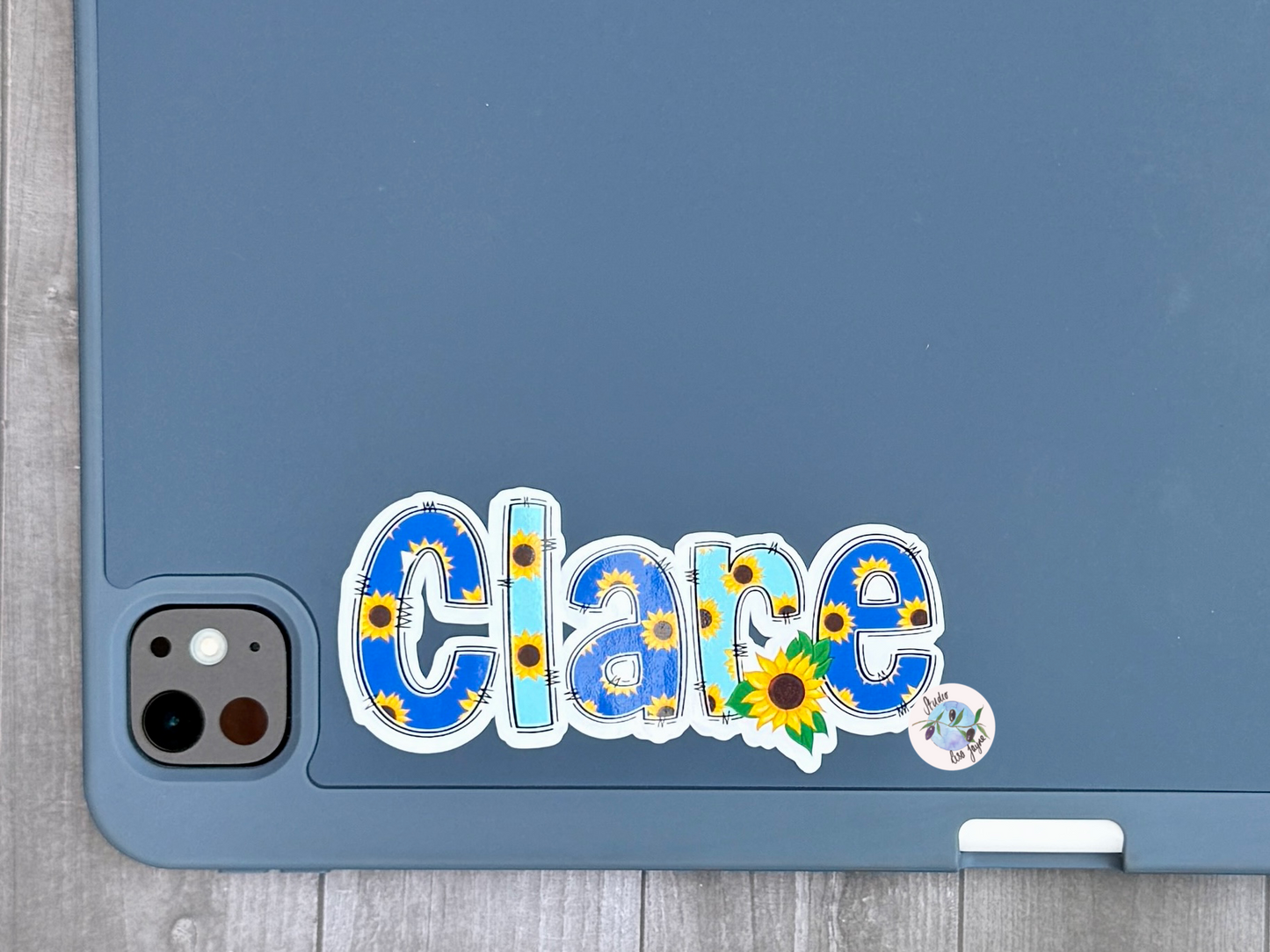 Sticker with 'Clare' and sunflower designs on a blue tablet iPad