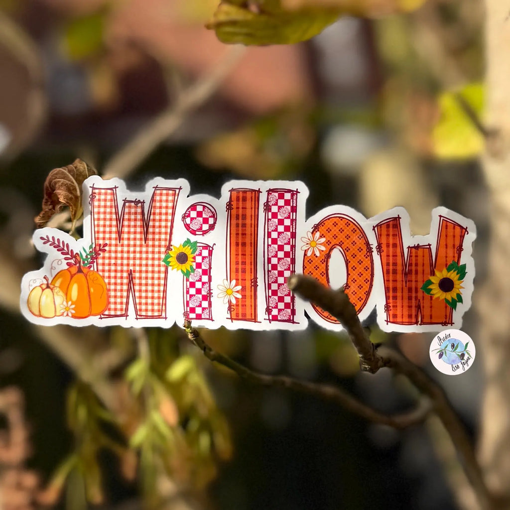 Autum decorative sticker with the word 'Willow' surrounded by autumn-themed illustrations on a blurred natural background.