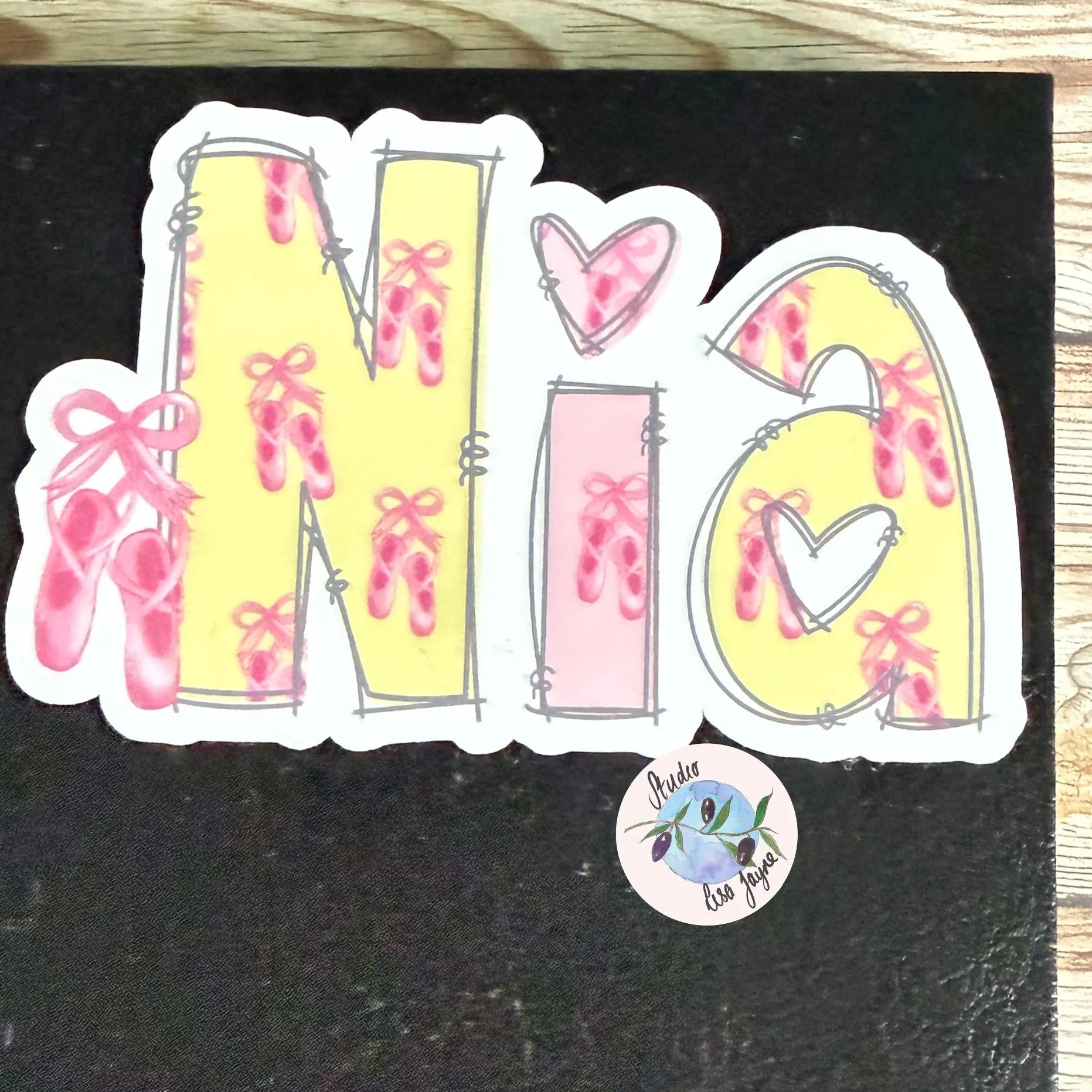 Sticker with 'Nia' design featuring ballet shoes and hearts on a black notebook, diary, journal