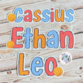 Colourful  letters spelling 'Cassius Ethan Leo' on a wooden background with basketball name sticker.