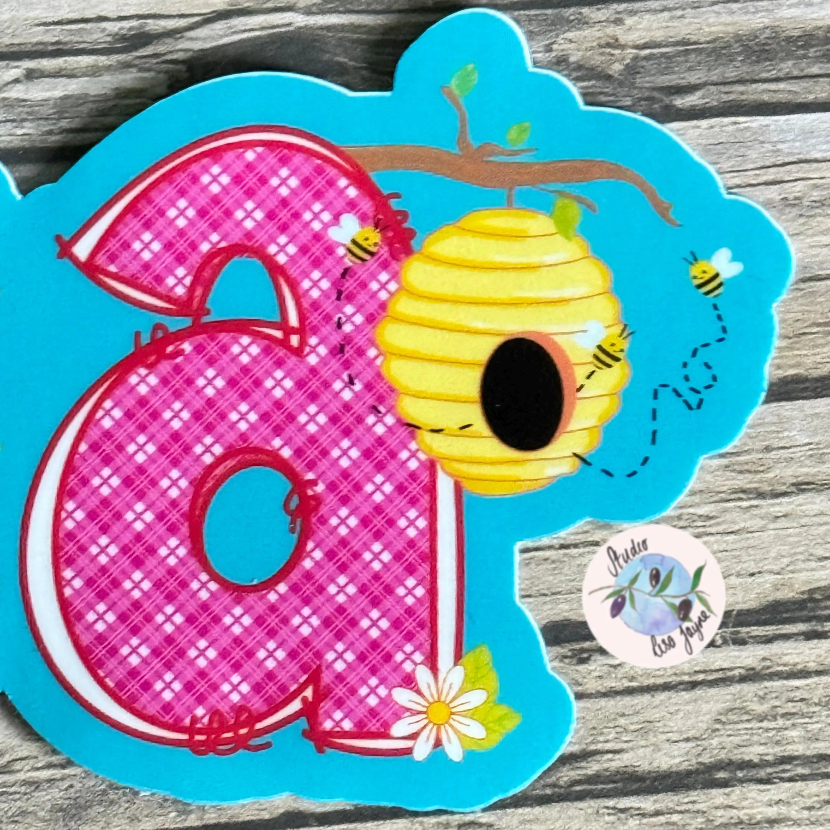 Decorative letter 'a' with a pink checkered pattern, yellow beehive, and bees on a blue background.