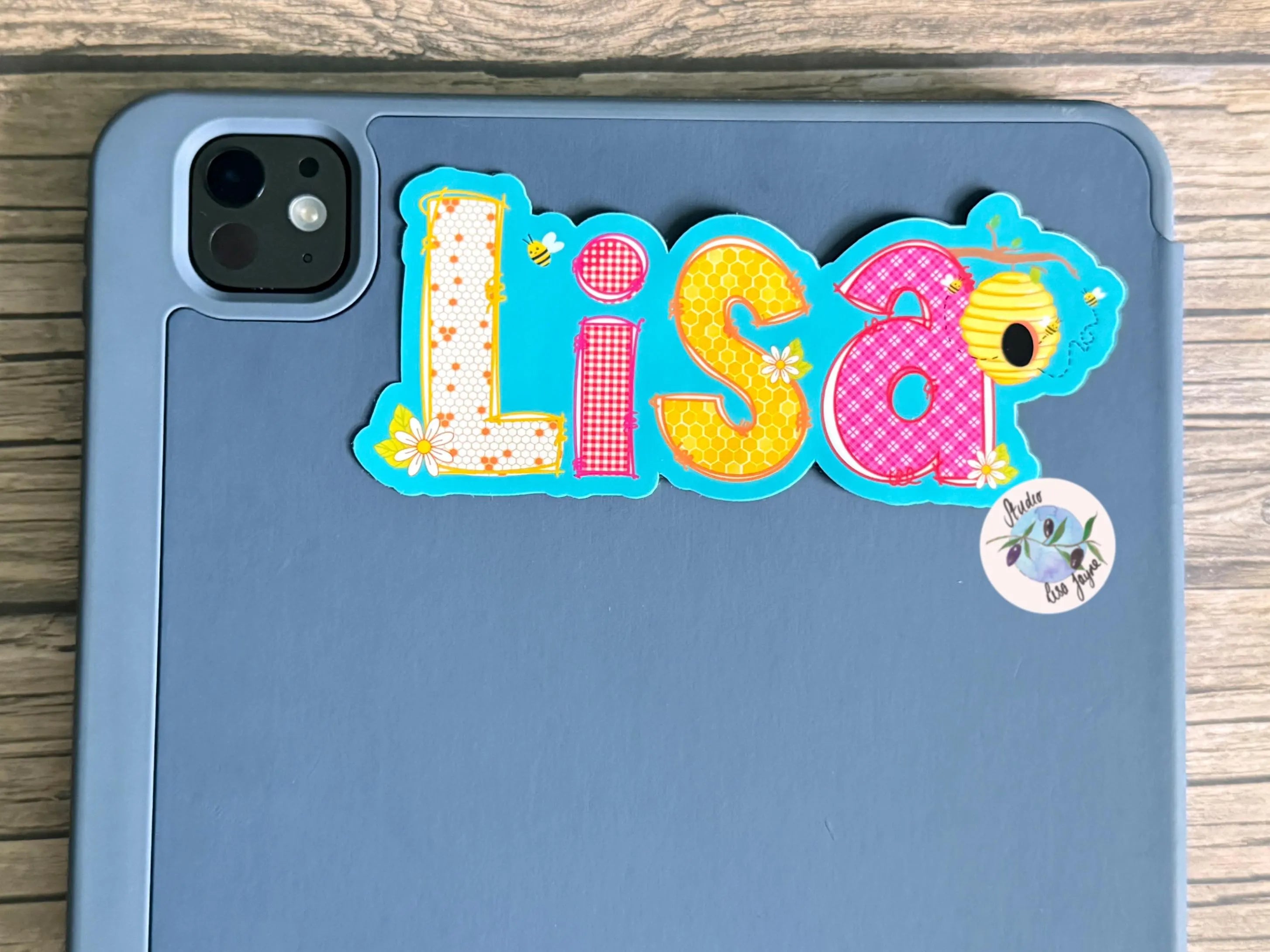 Colorful 'Lisa' picnic bees sticker on a blue tablet case with a wooden surface background