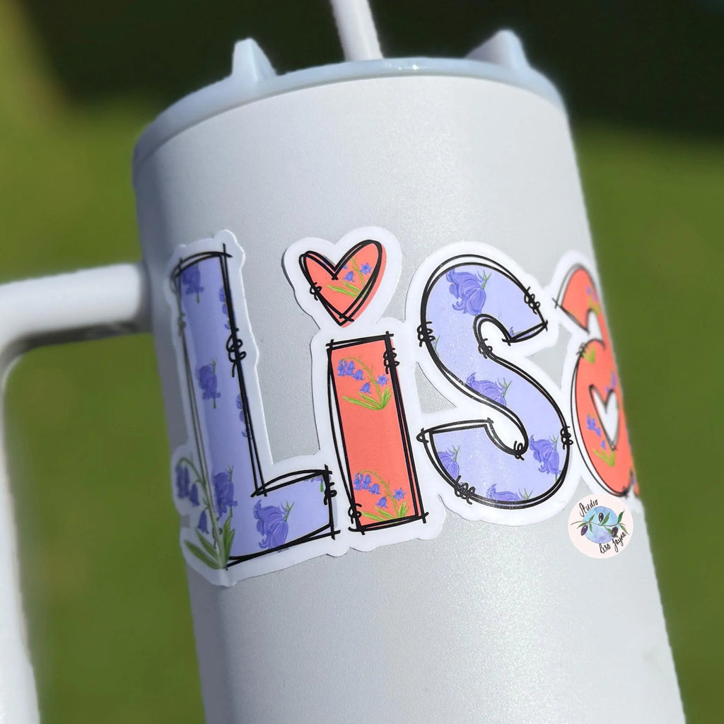 Tumbler with 'LISA' stickers on a water drink bottle with a blurred green background