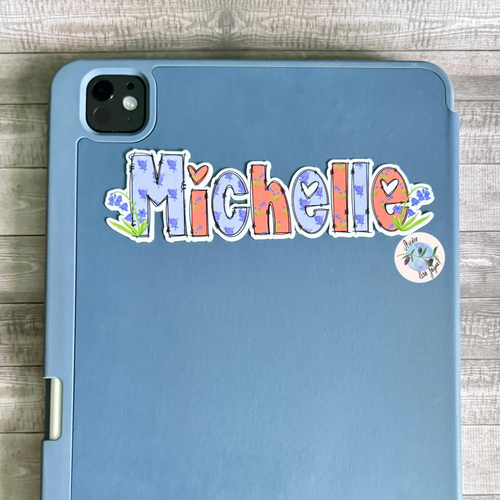 Blue tablet iPad case with 'Michelle' Bluebell sticker on a wooden surface