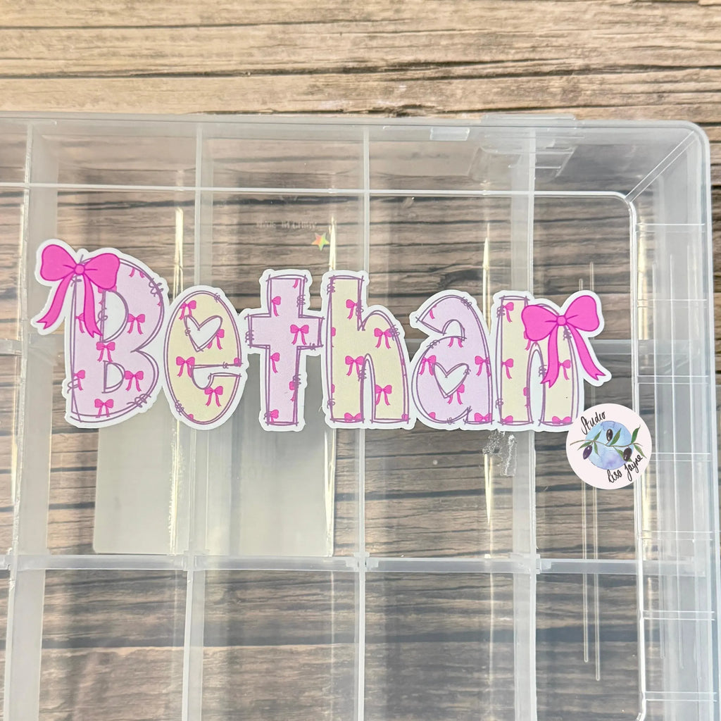 Clear plastic sweet treat box with decorative letters spelling 'Bethan' on a wooden surface