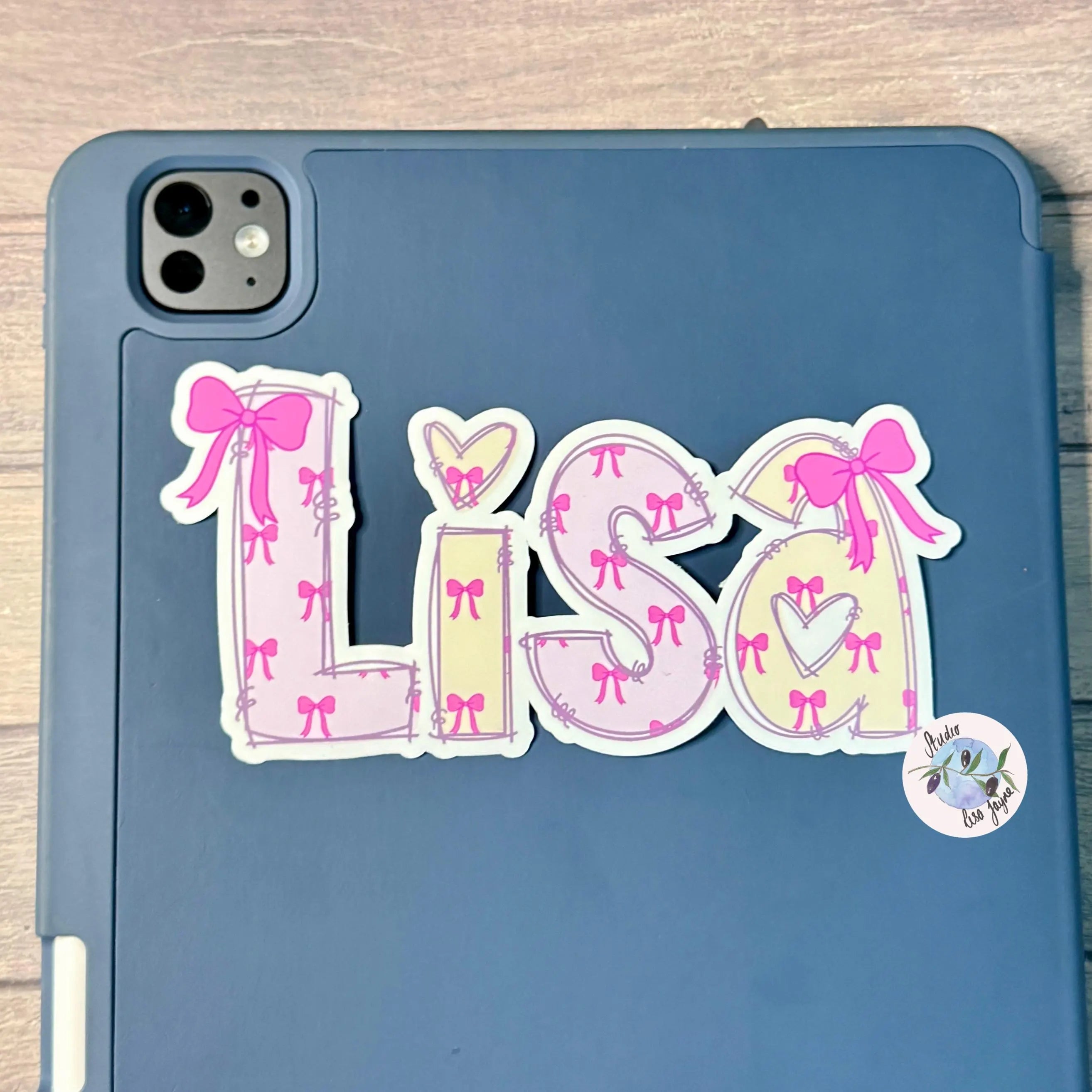 Blue iPad tablet with a decorative 'LISA' sticker featuring pink bows on a wooden surface