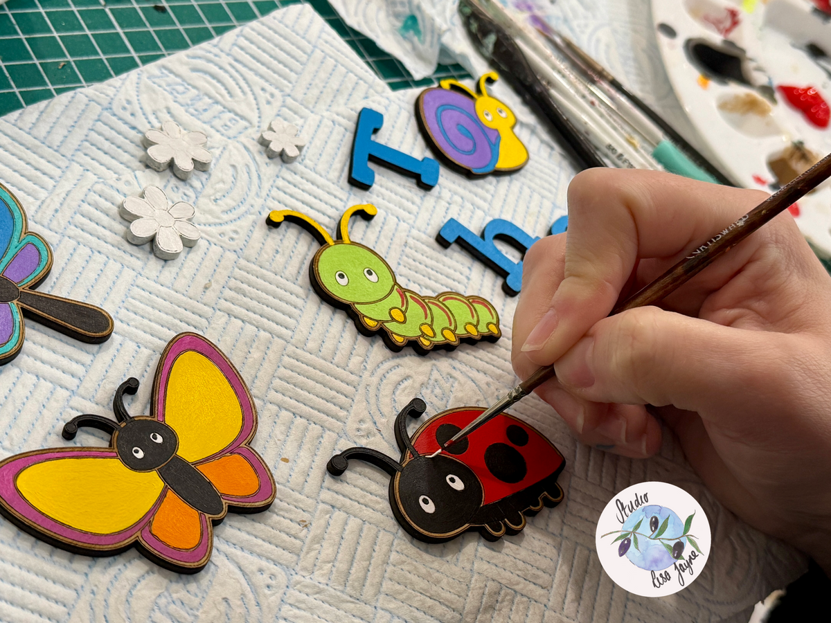 Hand painting a ladybug with colourful letters and shapes ready to be applied to a leaf shaped children’s bedroom plaque 