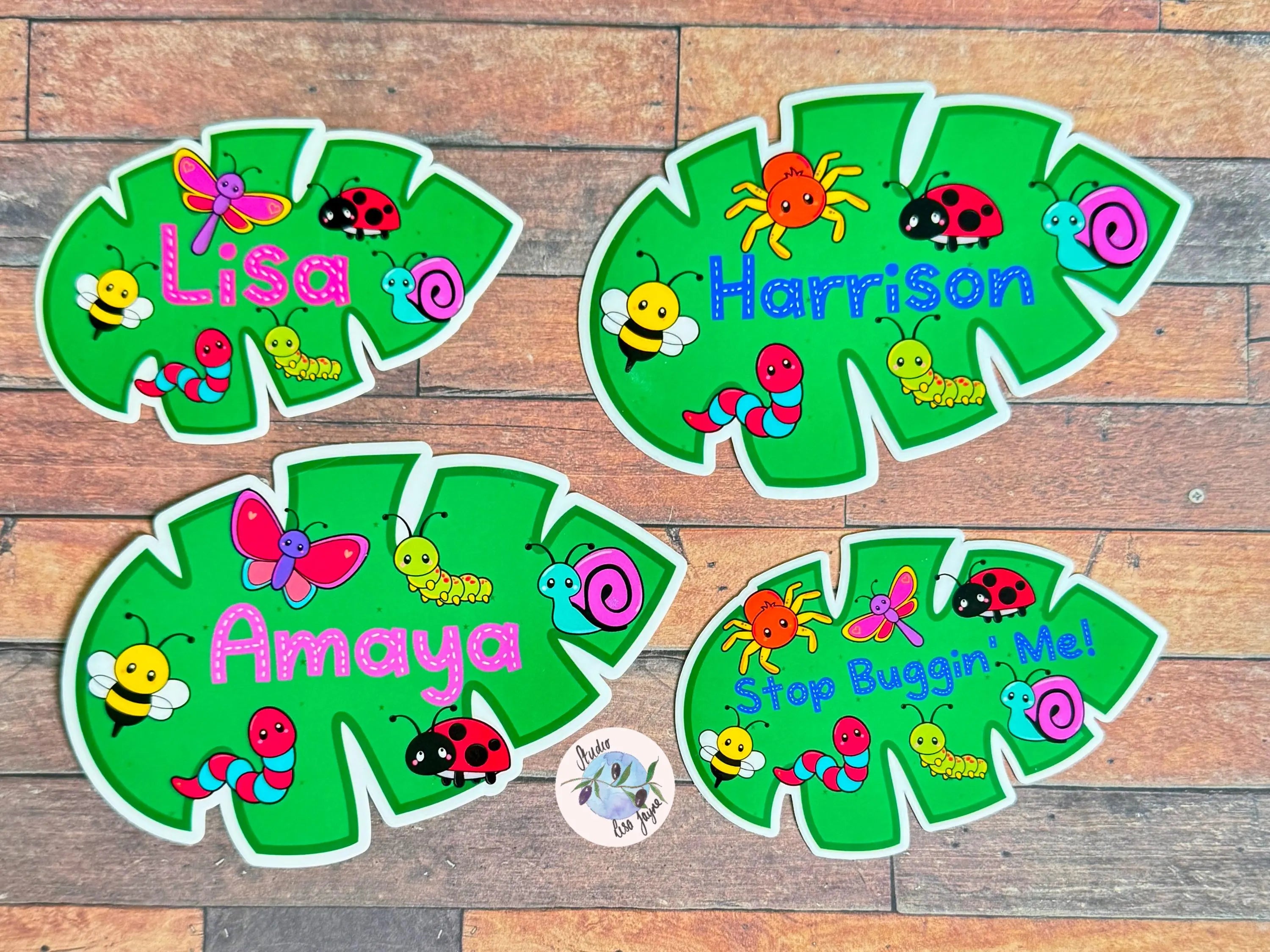 Four green name stickers with colorful insect designs on a wooden surface