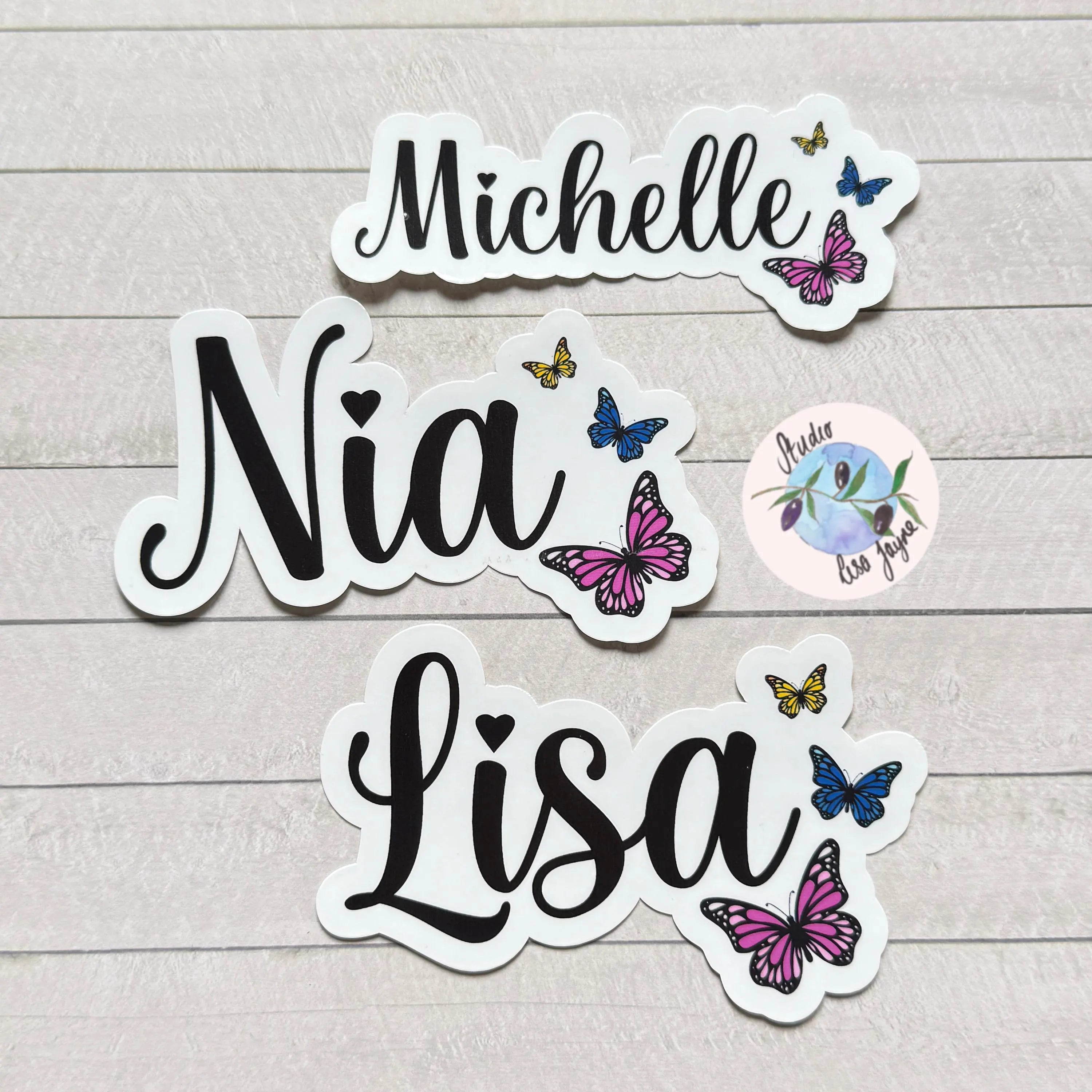 Stickers with names 'Michelle', 'Nia', and 'Lisa' along with colourfull elegant butterfly designs on a wooden surface.