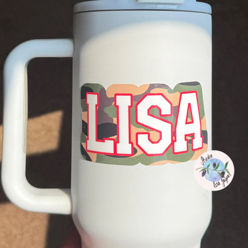 White mug with 'LISA' personliased camouflage sticker in colorful letters and a small sticker on a dark background