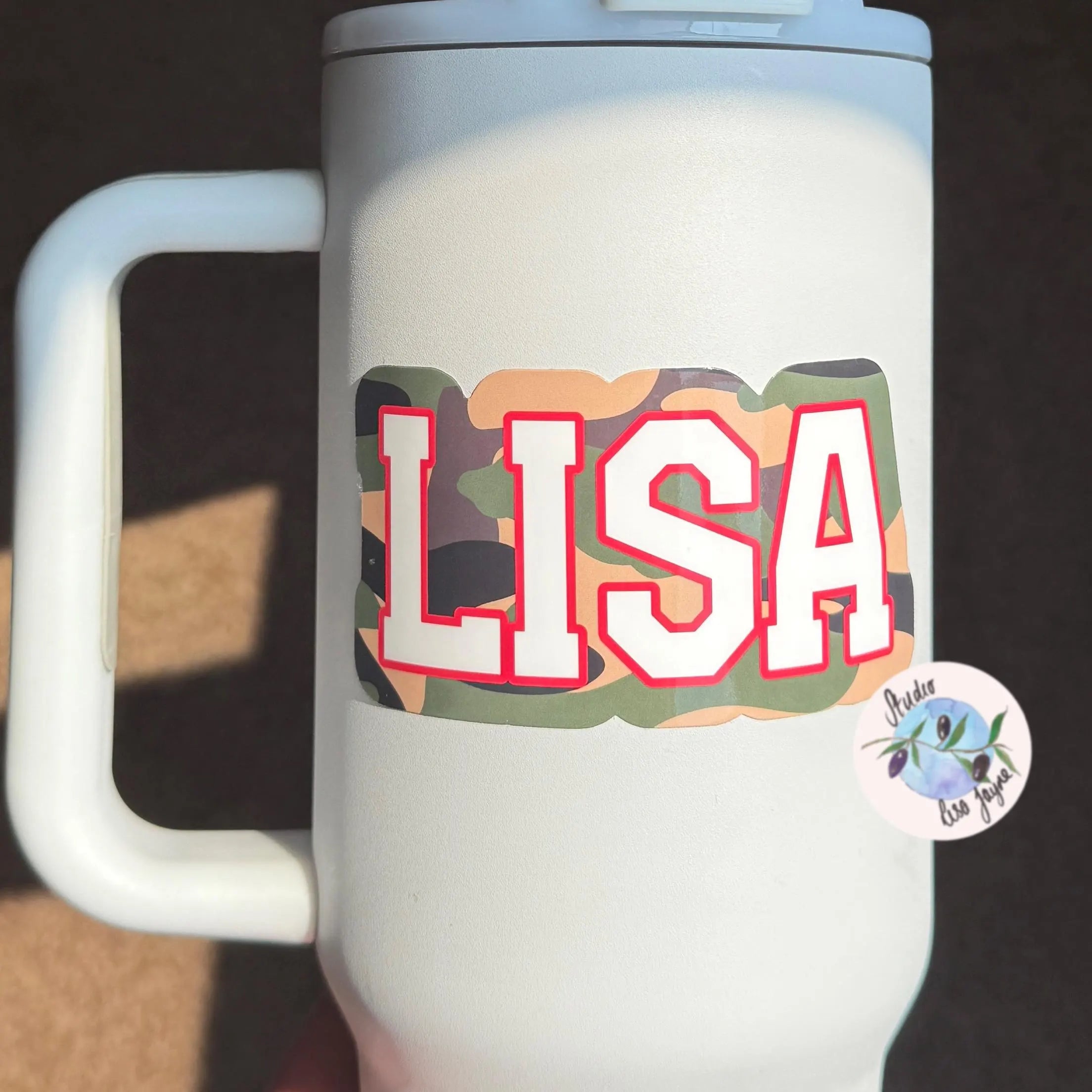 White mug with 'LISA' personliased camouflage sticker in colorful letters and a small sticker on a dark background