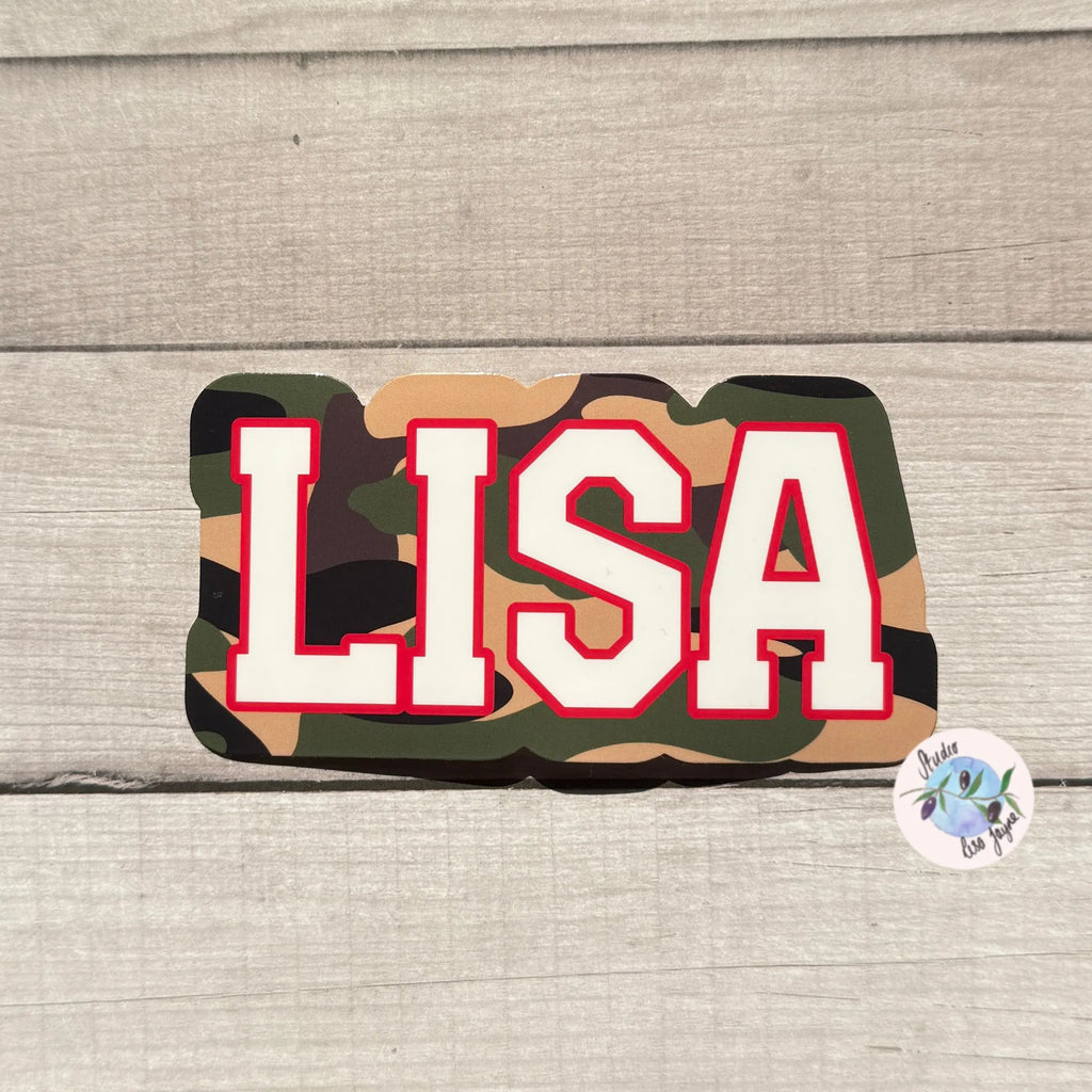 Camouflage-patterned name sticker decal with 'LISA' in white letters on a wooden surface