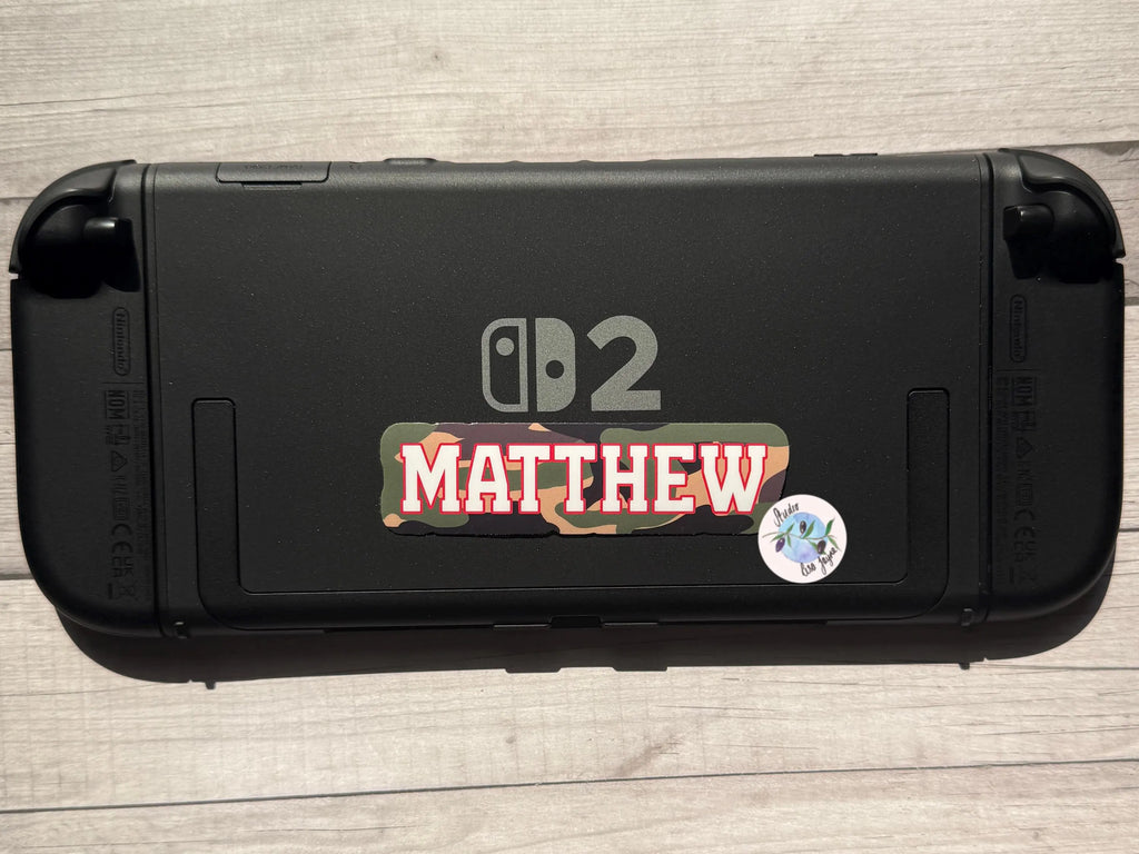 Black gaming console with 'Matthew' camouflage sticker on a wooden surface.  Nintendo Switch 2