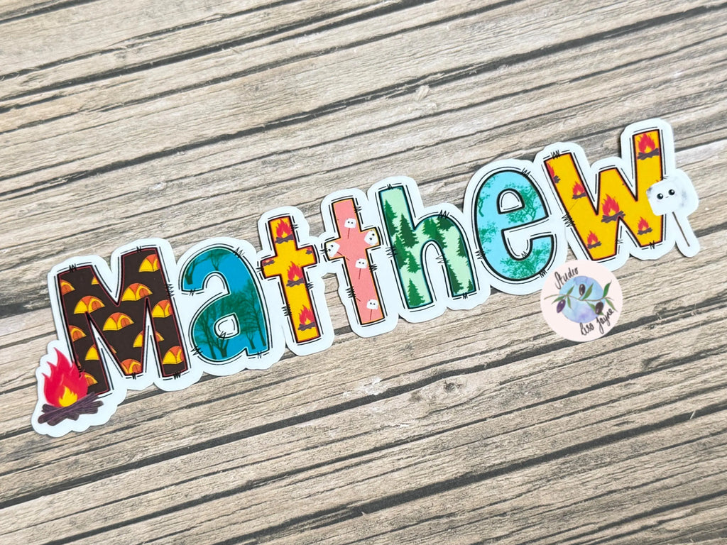 Colorful camping sticker with 'Matthew' name on a wooden surface.  Campfire, toasted marshmallow