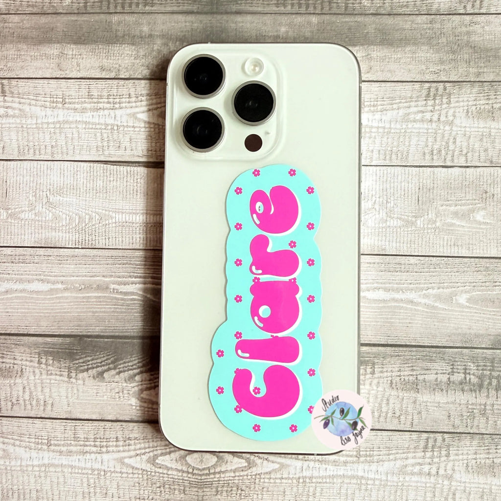Phone case with pink cherry blossom decal with light green background, placed on a wooden surface.