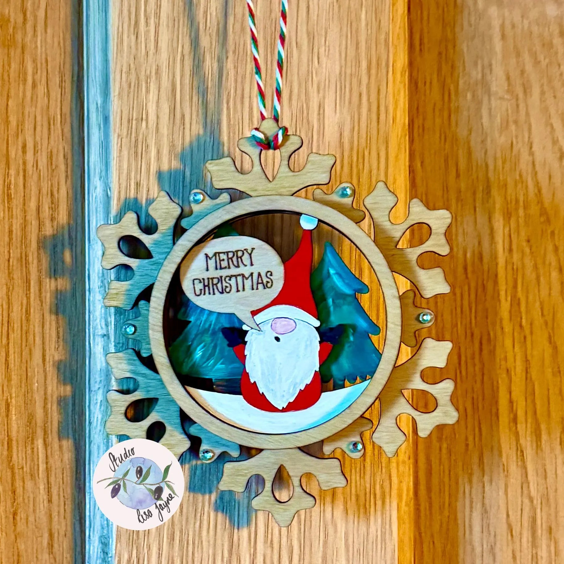 Christmas ornament with a Sants gnome and 'Merry Christmas' text on a wooden surface