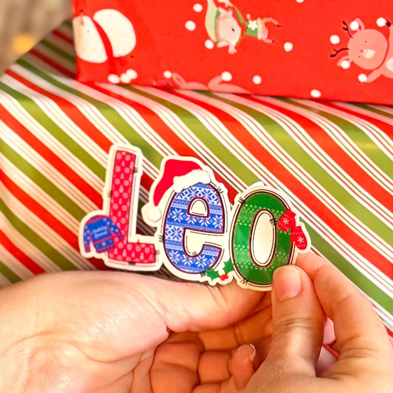 Colorful 'Leo' name label held over a Christmas-themed background with striped paper.