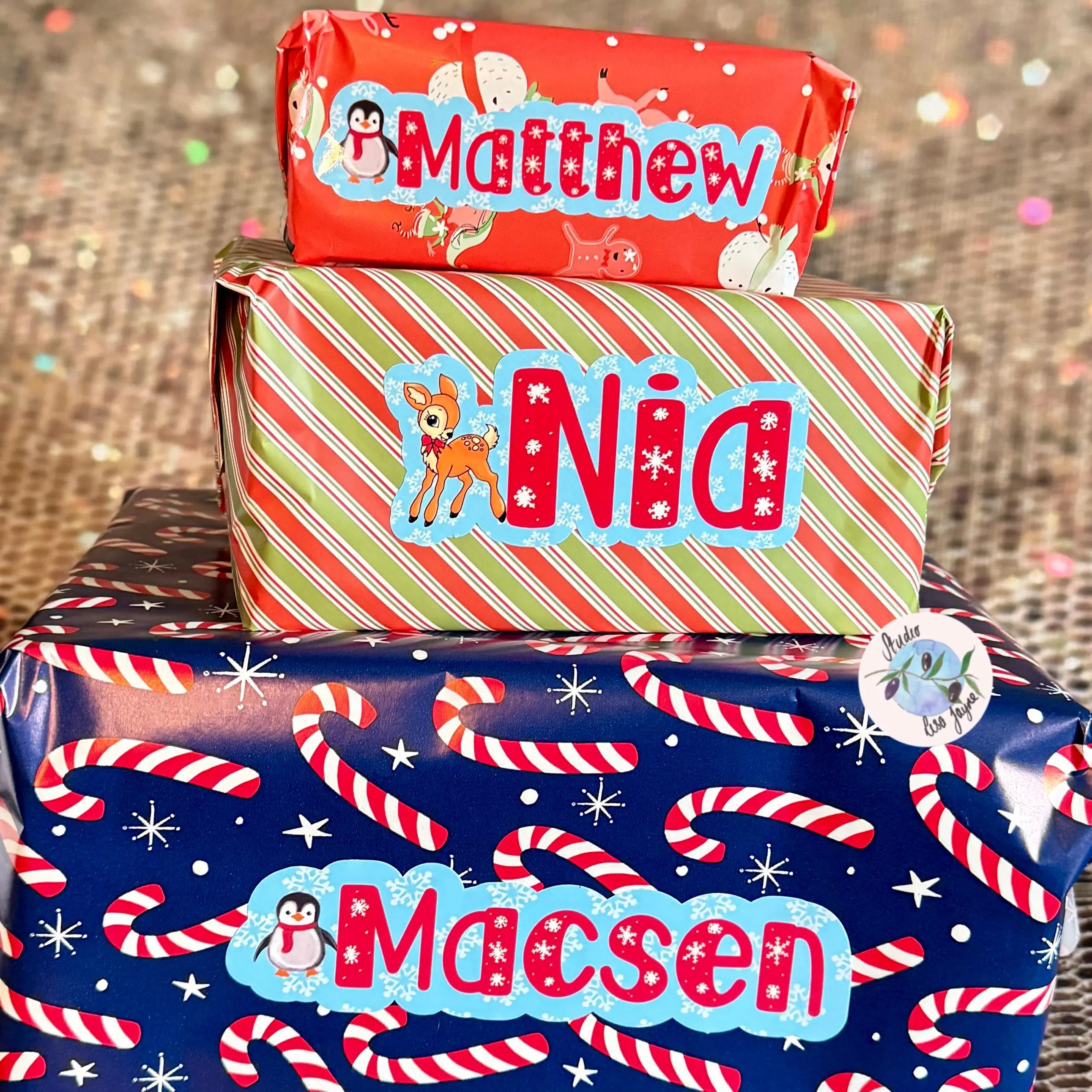 Three wrapped gifts with personalized name stickers with a snowflake, reindeer and penguin theme on a glittery background