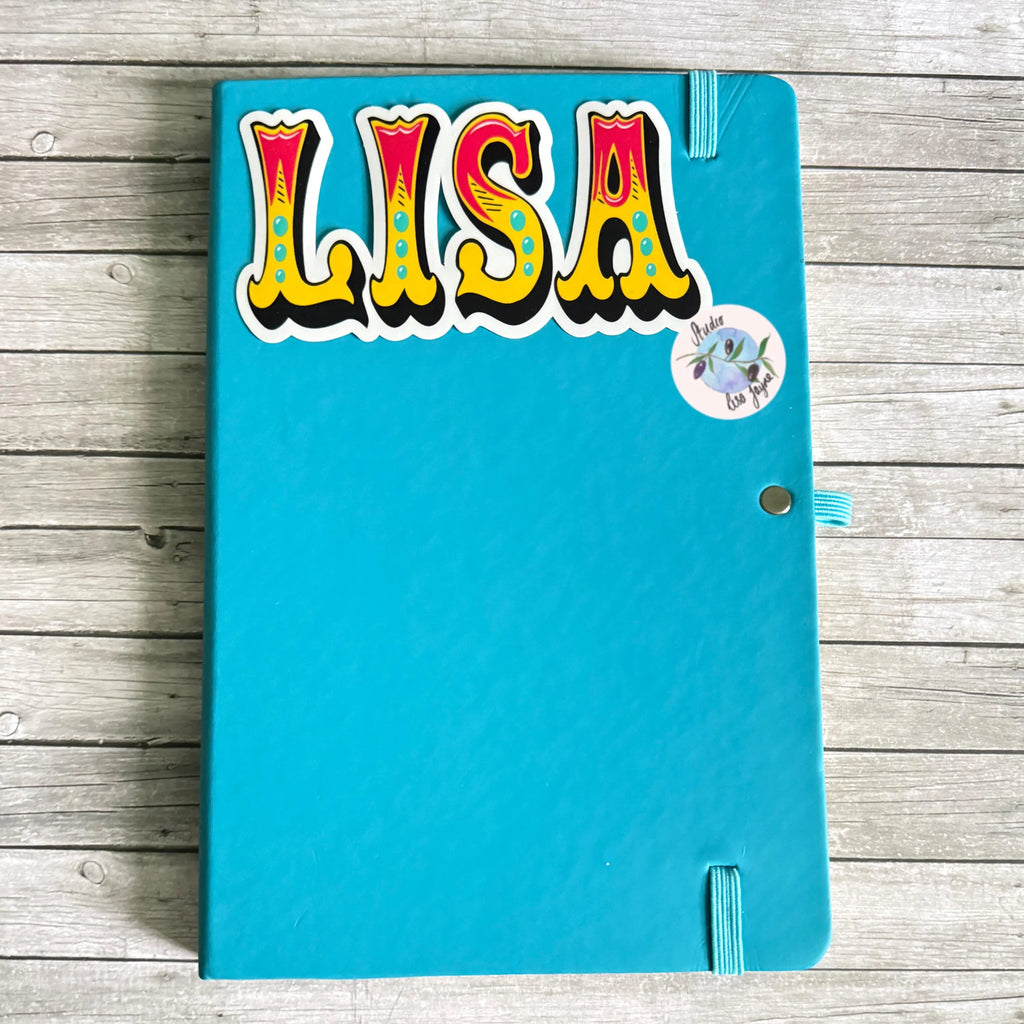 Blue notebook with colorful 'LISA' old style funfair name sticker on a wooden surface