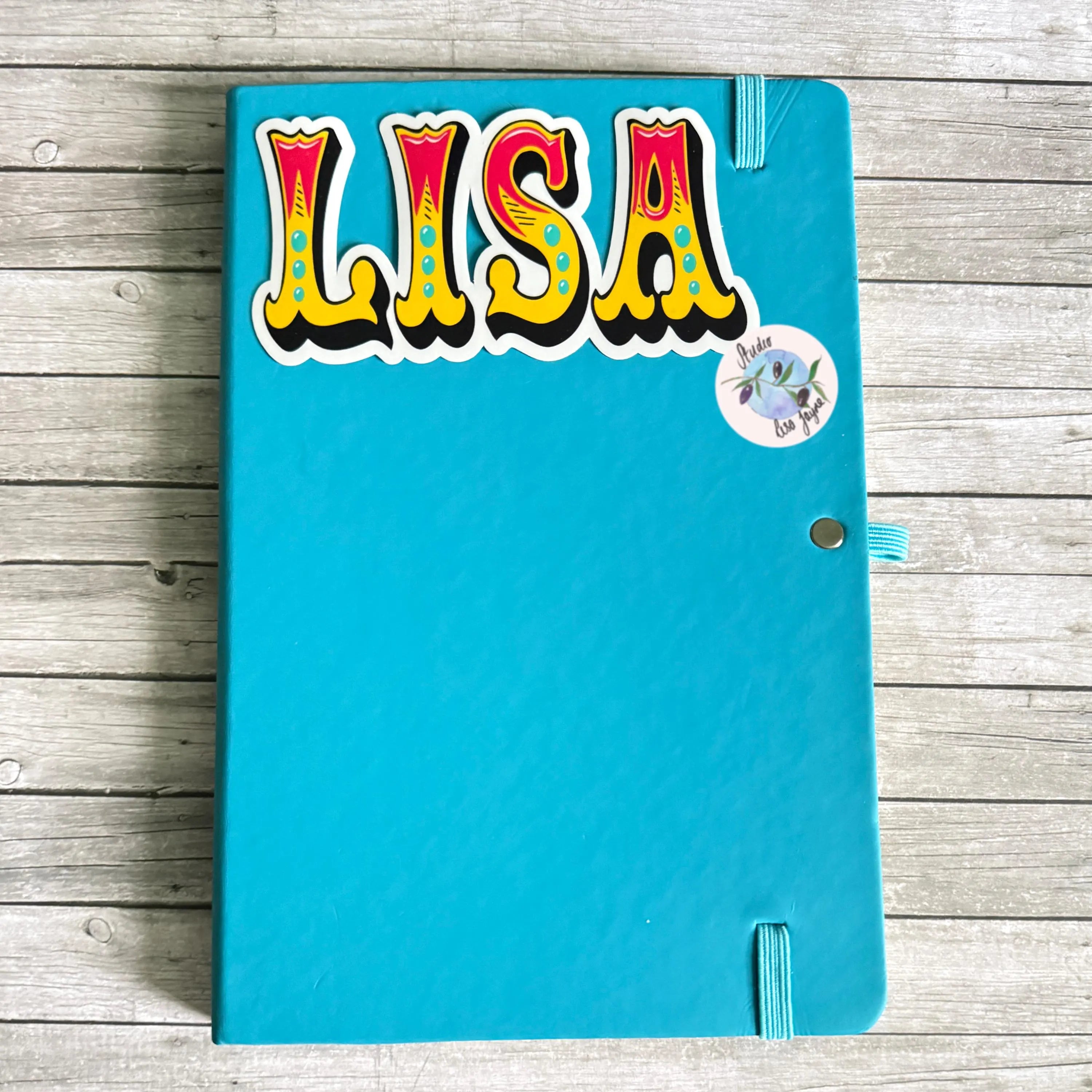 Blue notebook with colorful 'LISA' old style funfair name sticker on a wooden surface