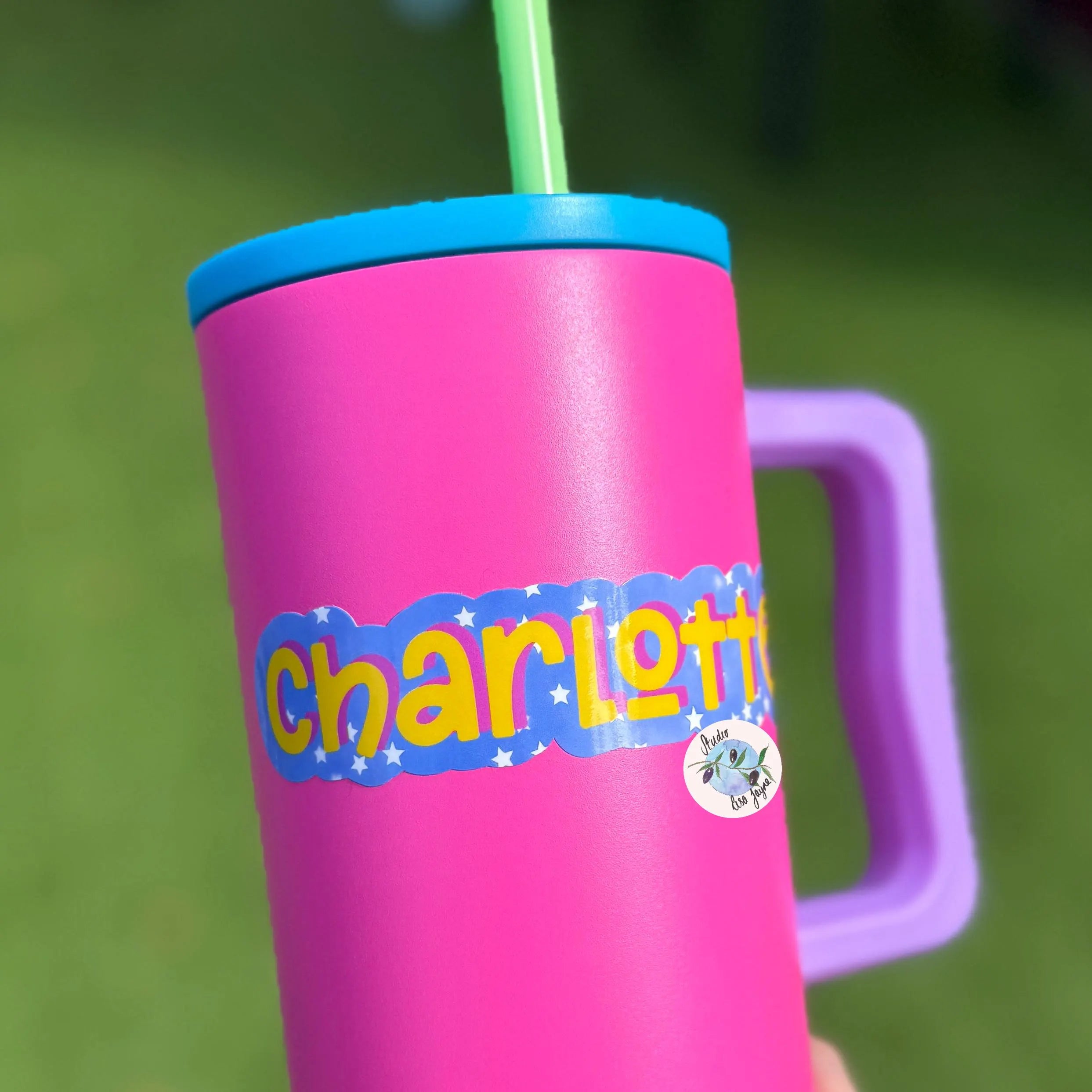 Pink mug with 'charlotte' cute star sticker and purple handle against a green background