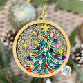 Decorative Christmas tree ornament with colorful gemstones on a wooden base, surrounded by greenery.