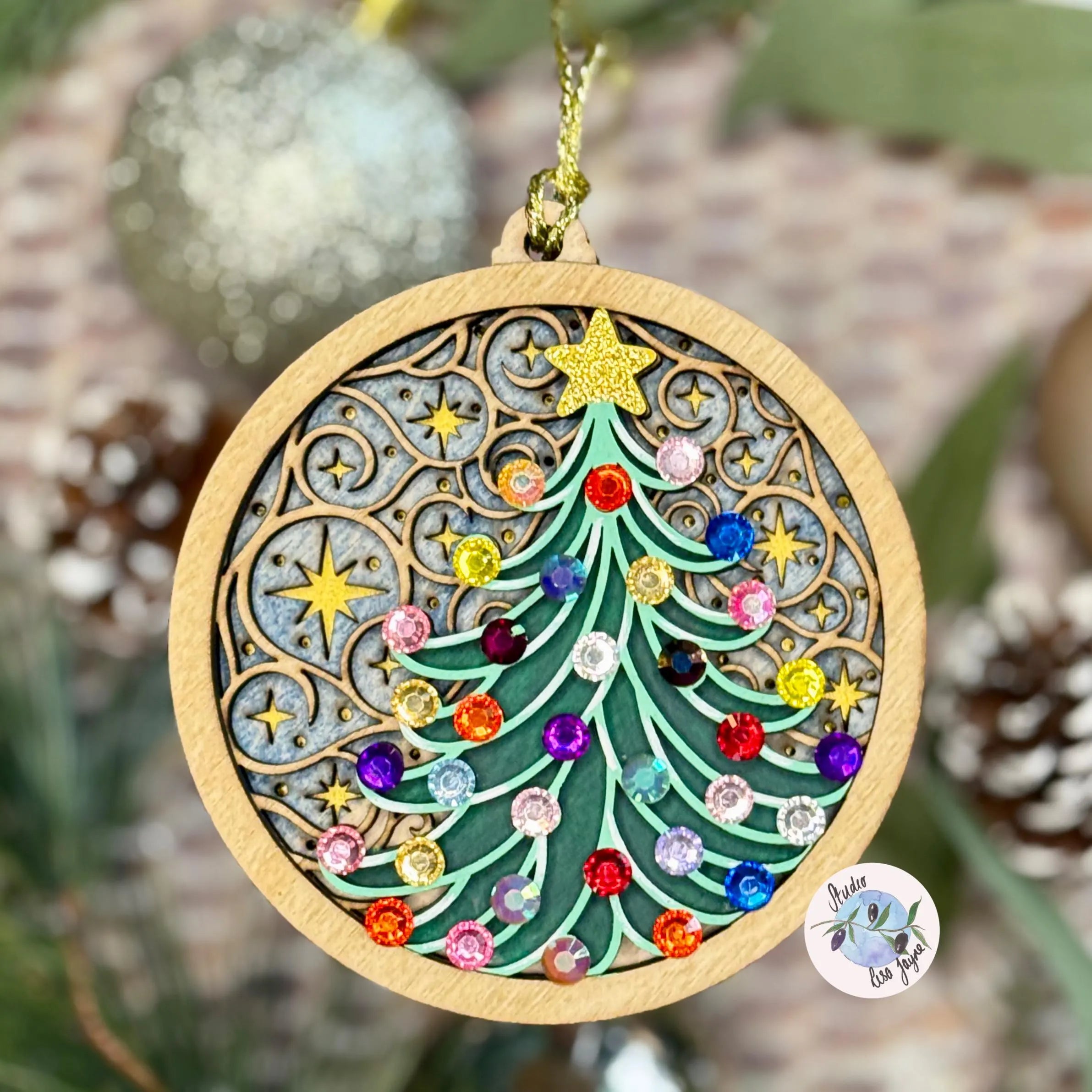 Decorative Christmas tree ornament with colorful gemstones on a wooden base, surrounded by greenery.
