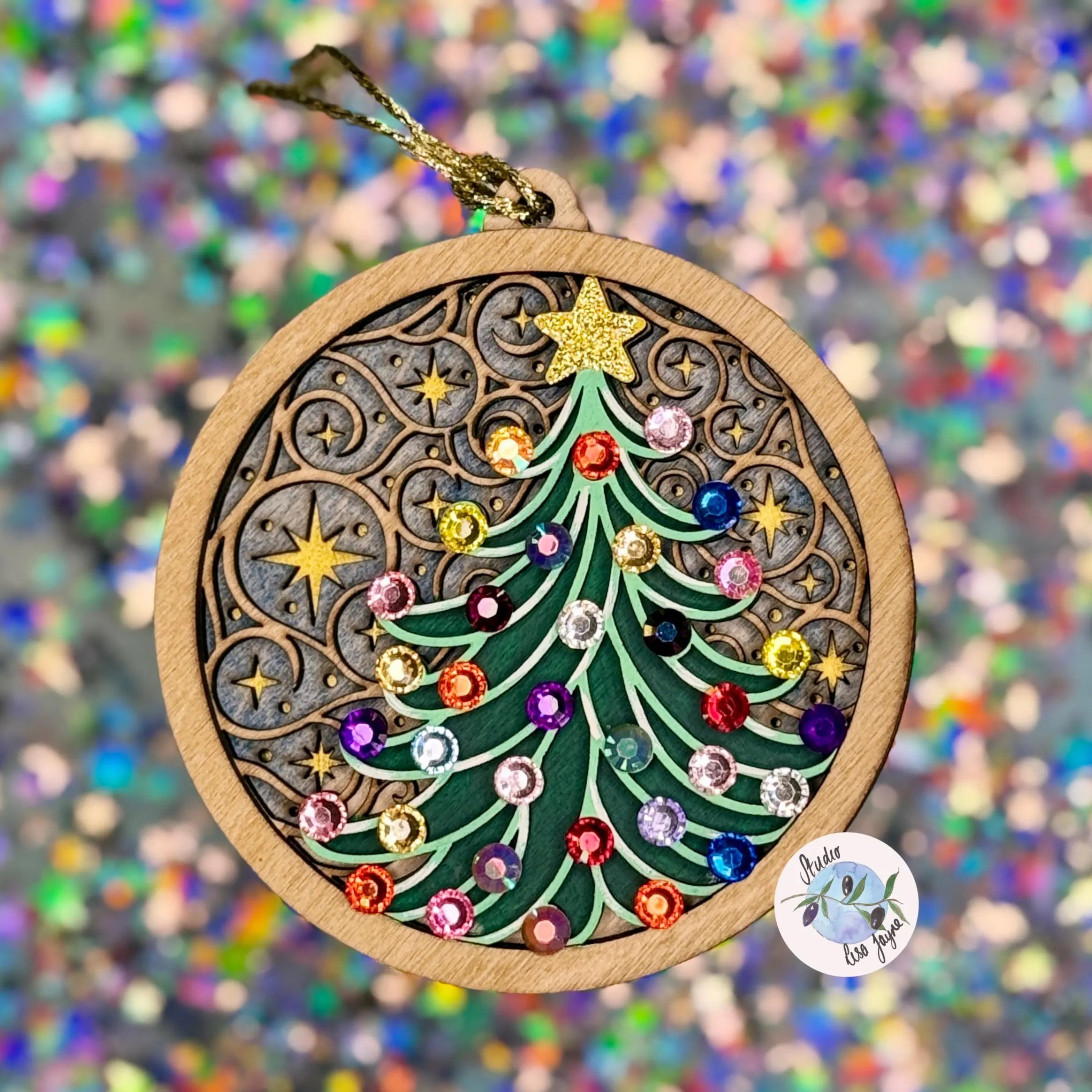 Handmade and painted Christmas tree ornament with colorful Diamantés on a wooden painted and stained layered base against a glittered blurred background.