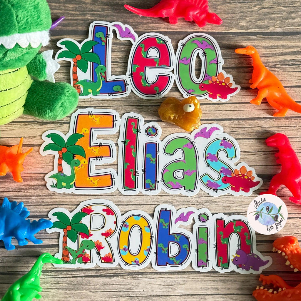 Colorful name stickers with dinosaur design stickers on a wooden surface with toy dinosaurs.