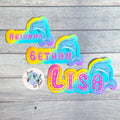 Colorful rainbow stickers with names and dolphin designs on a wooden surface