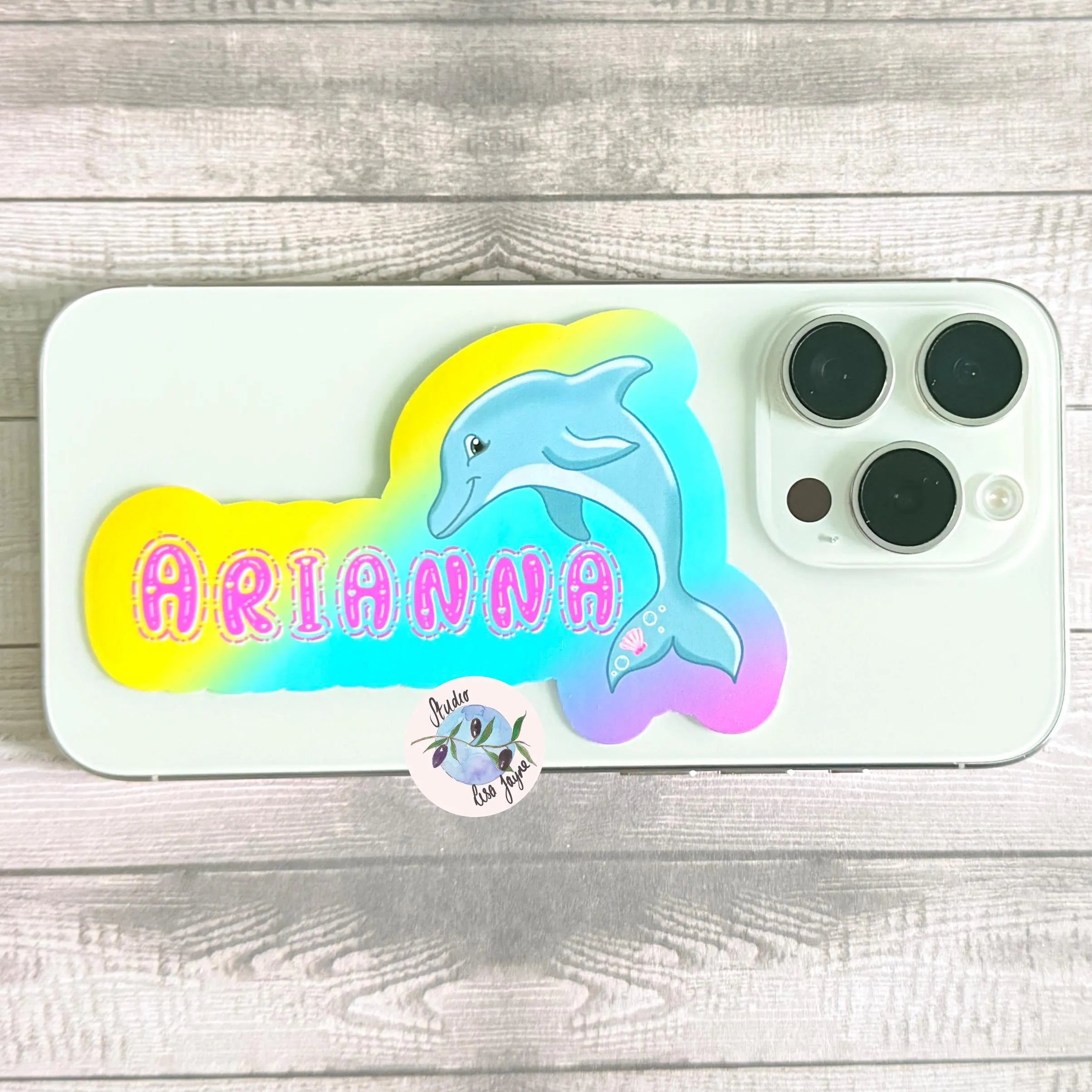 iPhone with dolphin sticker design with 'ARIANNA' pink text on a rainbow backdrop