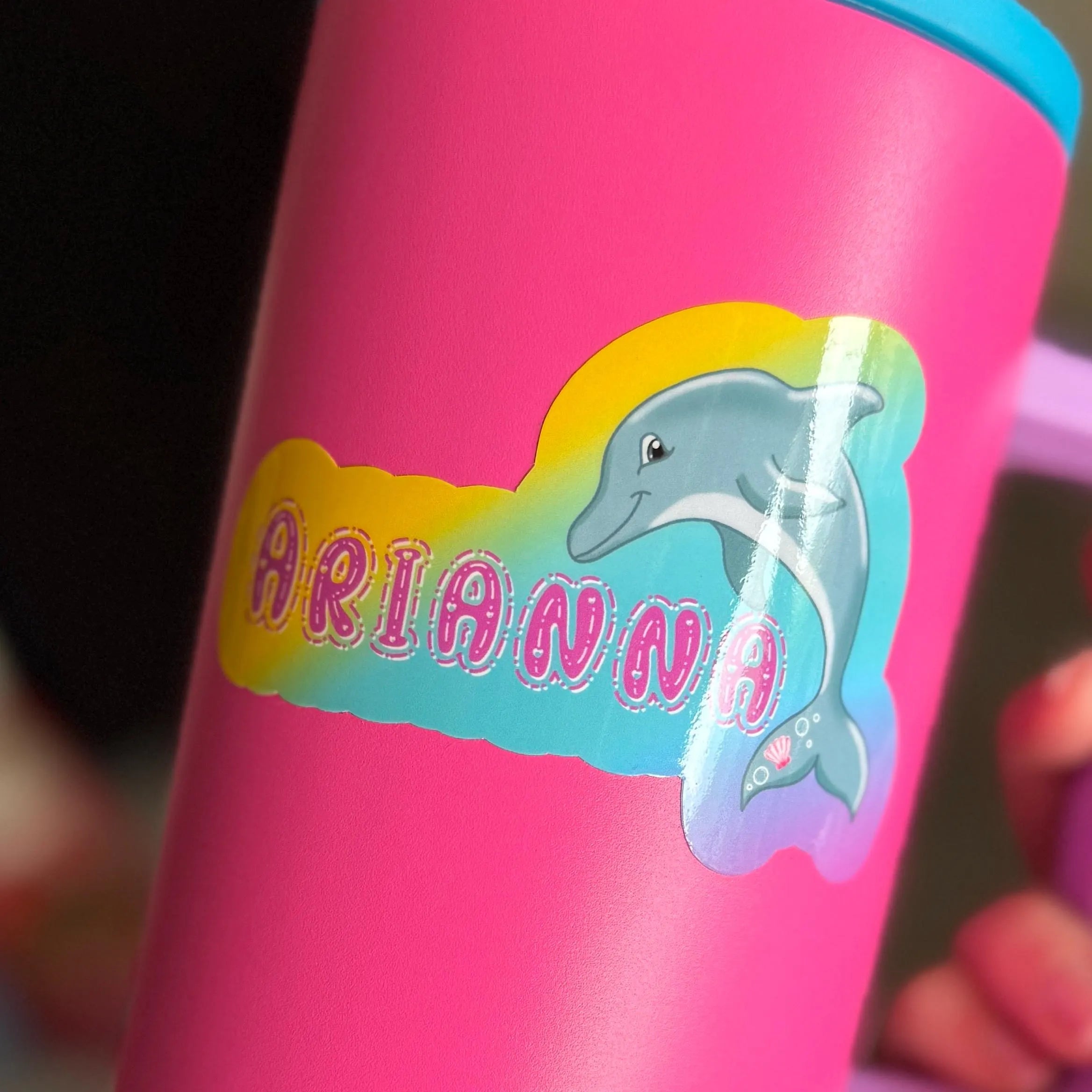 Pink water bottle with dolphin sticker design with 'ARIANNA' text on a rainbow background