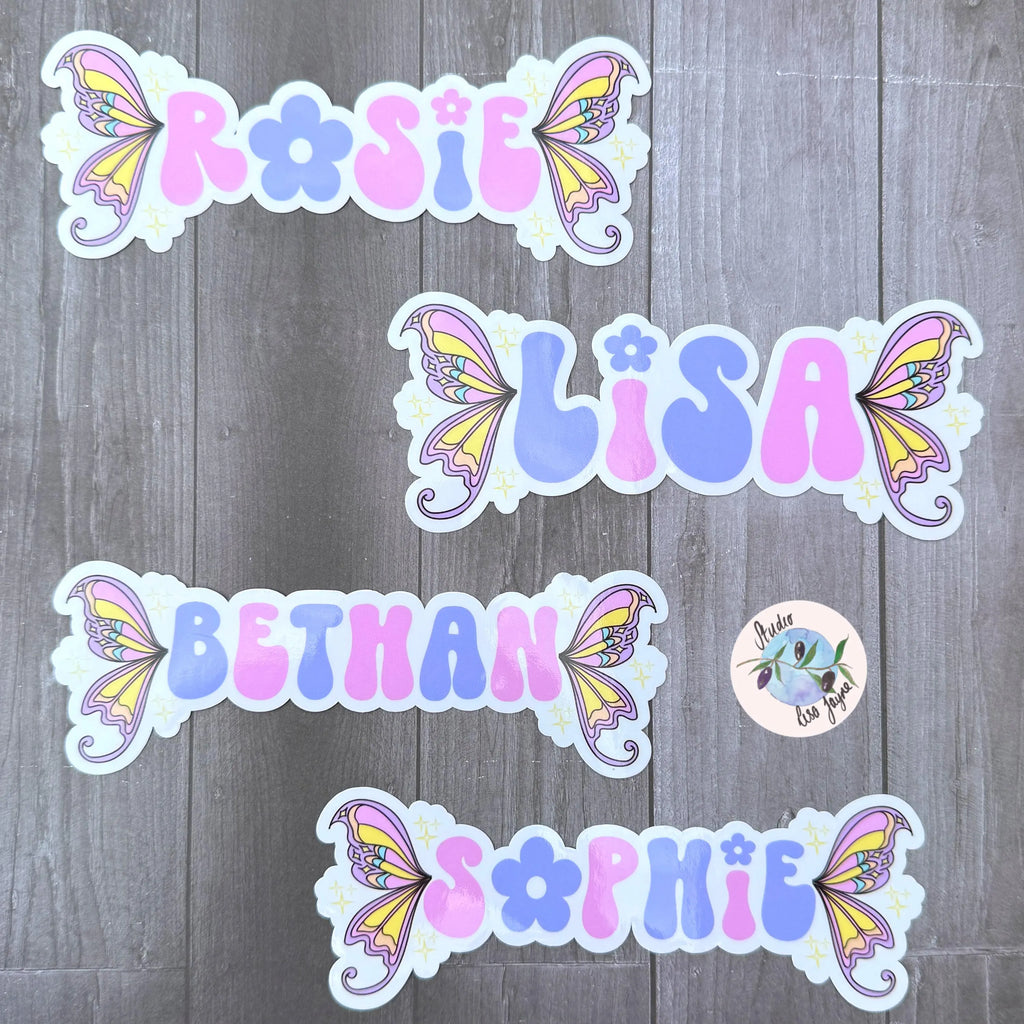 Stickers with colorful fairy wing designs and names on a wooden surface