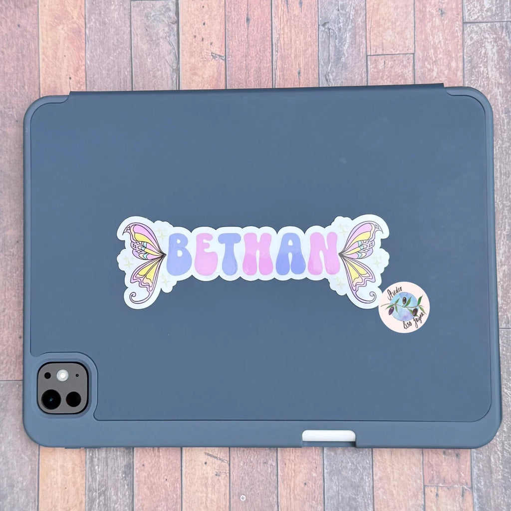 Dark blue iPad tablet case with 'BETHAN' and fairy wing designed stcker on a wooden surface