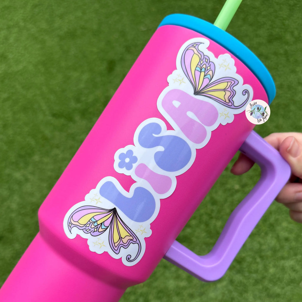 Pink tumbler with 'Lisa' and fairy wing designs on a green background
