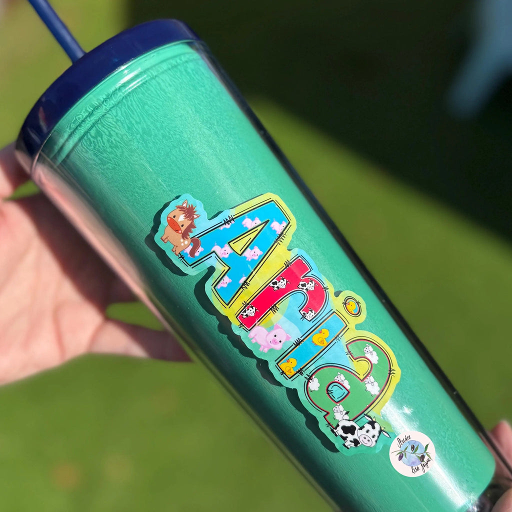 Green tumbler with colorful design and text animal farm sticker held by a hand against a green background