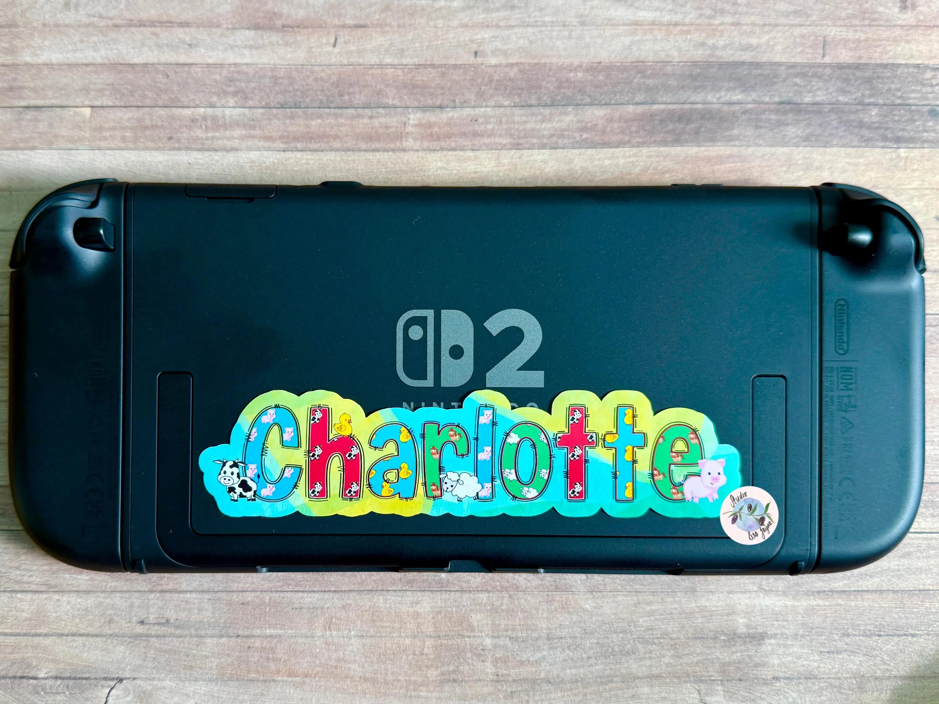 Black Nintendo Switch gaming console with colorful 'Charlotte' Farm animal decal on a wooden surface