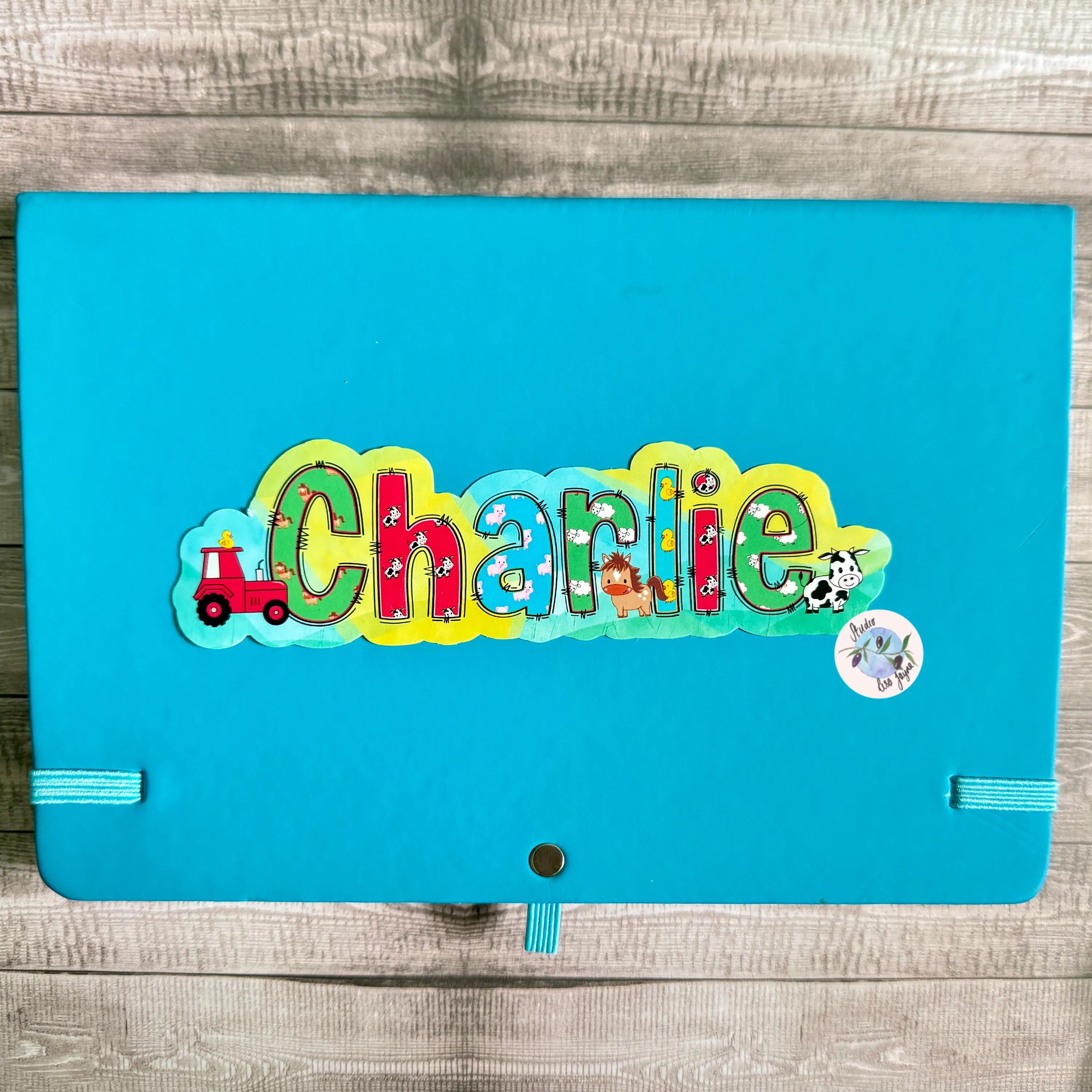 Blue notebook diary with colorful 'Charlie' animal farm design on a wooden surface