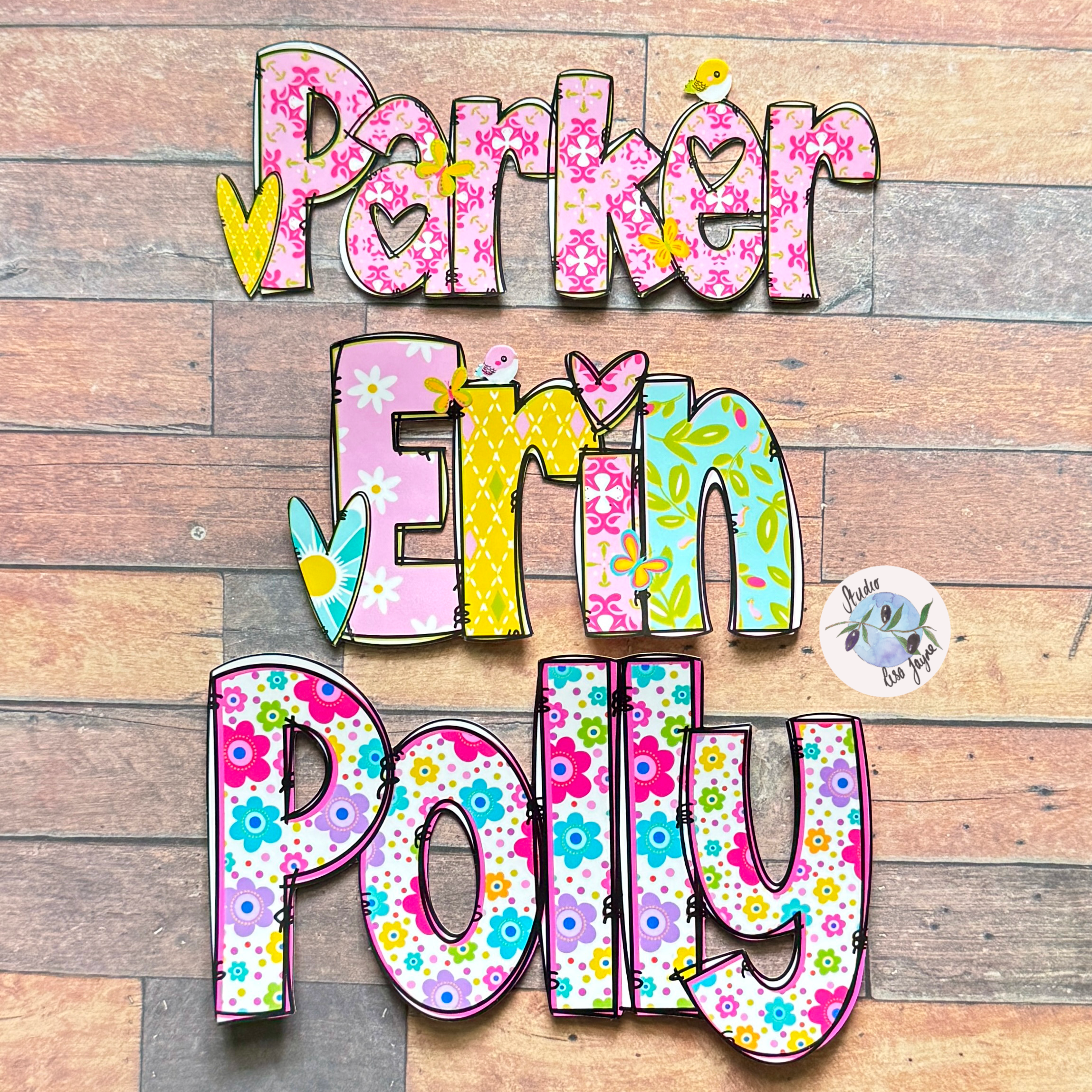 Personalised flower name stickers spelling 'Parker Erin Polly' with colourful floral patterns and heart details, displayed on a rustic wood plank background.
