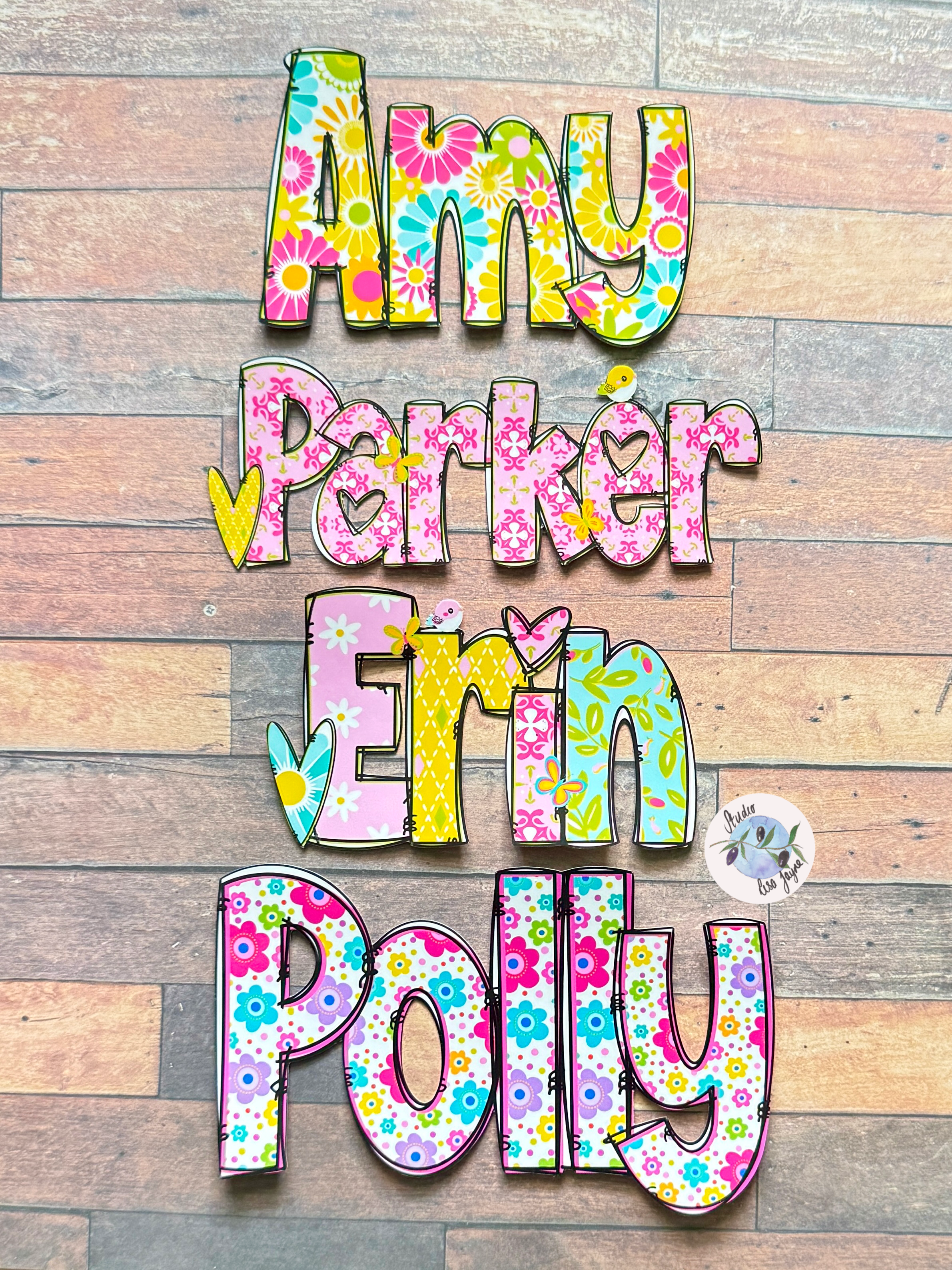 Personalised flower name stickers spelling 'Amy Parker Erin Polly' in a colourful floral pattern, displayed against a rustic wood plank background.