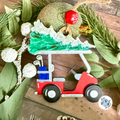 Christmas decoration of a red golf cart with a green xmas tree on a wooden surface with greenery.