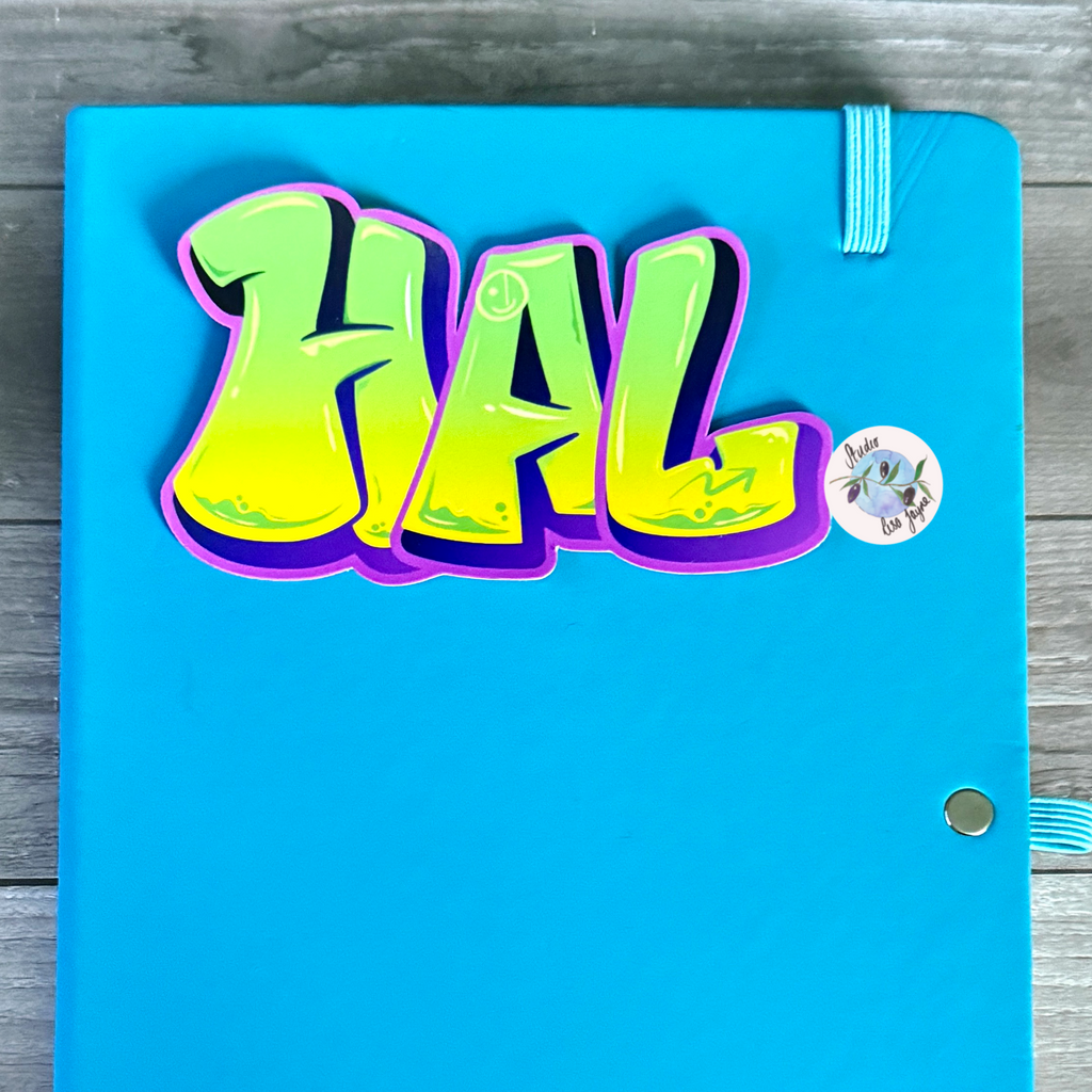 Blue notebook with a colorful graffiti slime 'HAL' sticker on a wooden surface.  Green, Purple