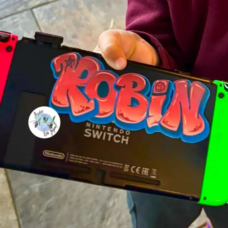 Red graffiti name sticker in the name Robin applied to a Nintendo Switch gaming console