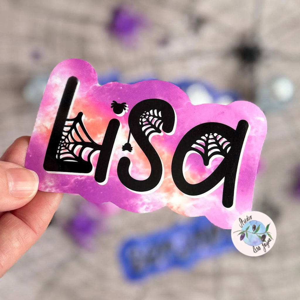 Hand holding a pink and orange colorful name tag with 'Lisa' in a halloween themed font with spider webs