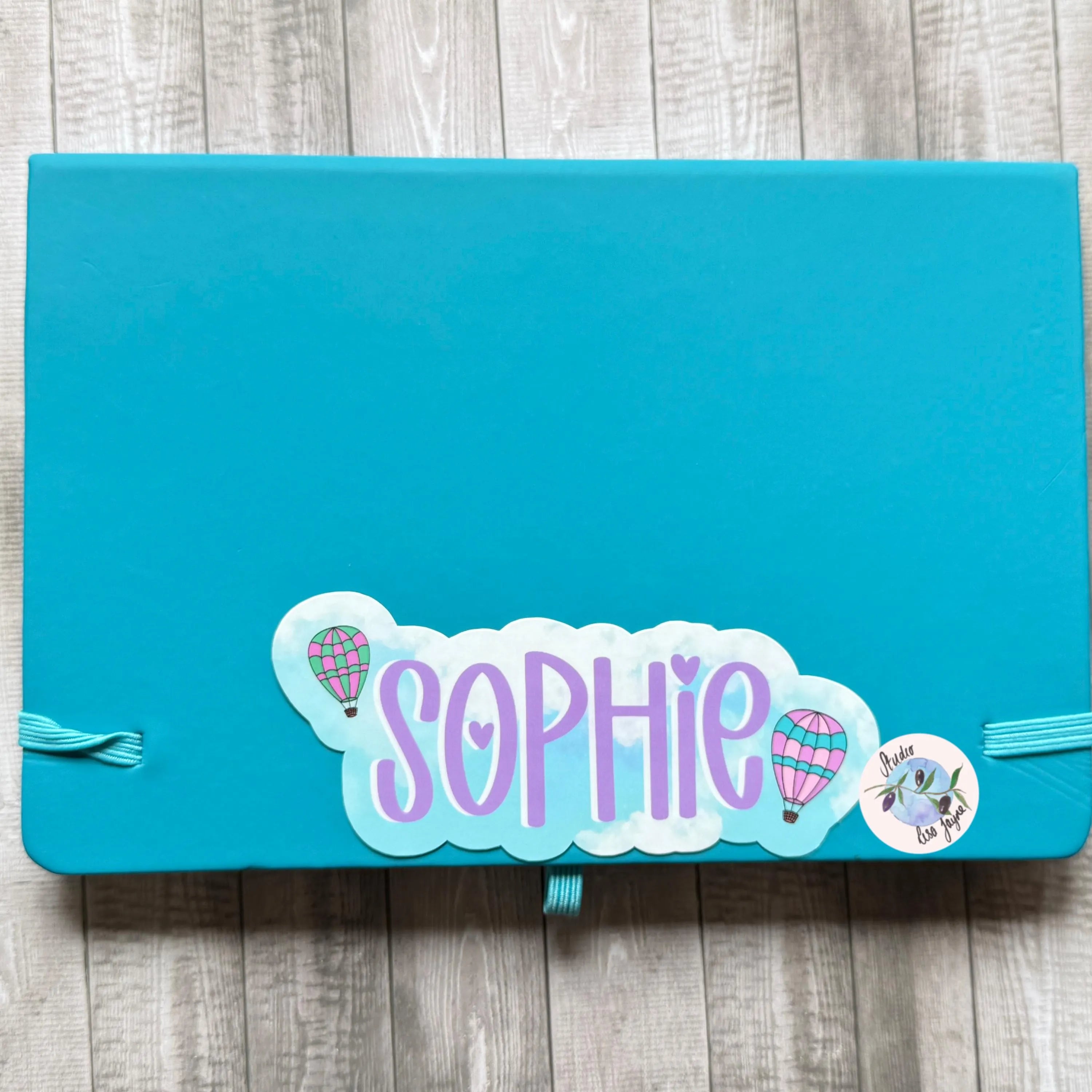 Blue notebook with 'Sophie' hot air baloon sticker on a wooden surface