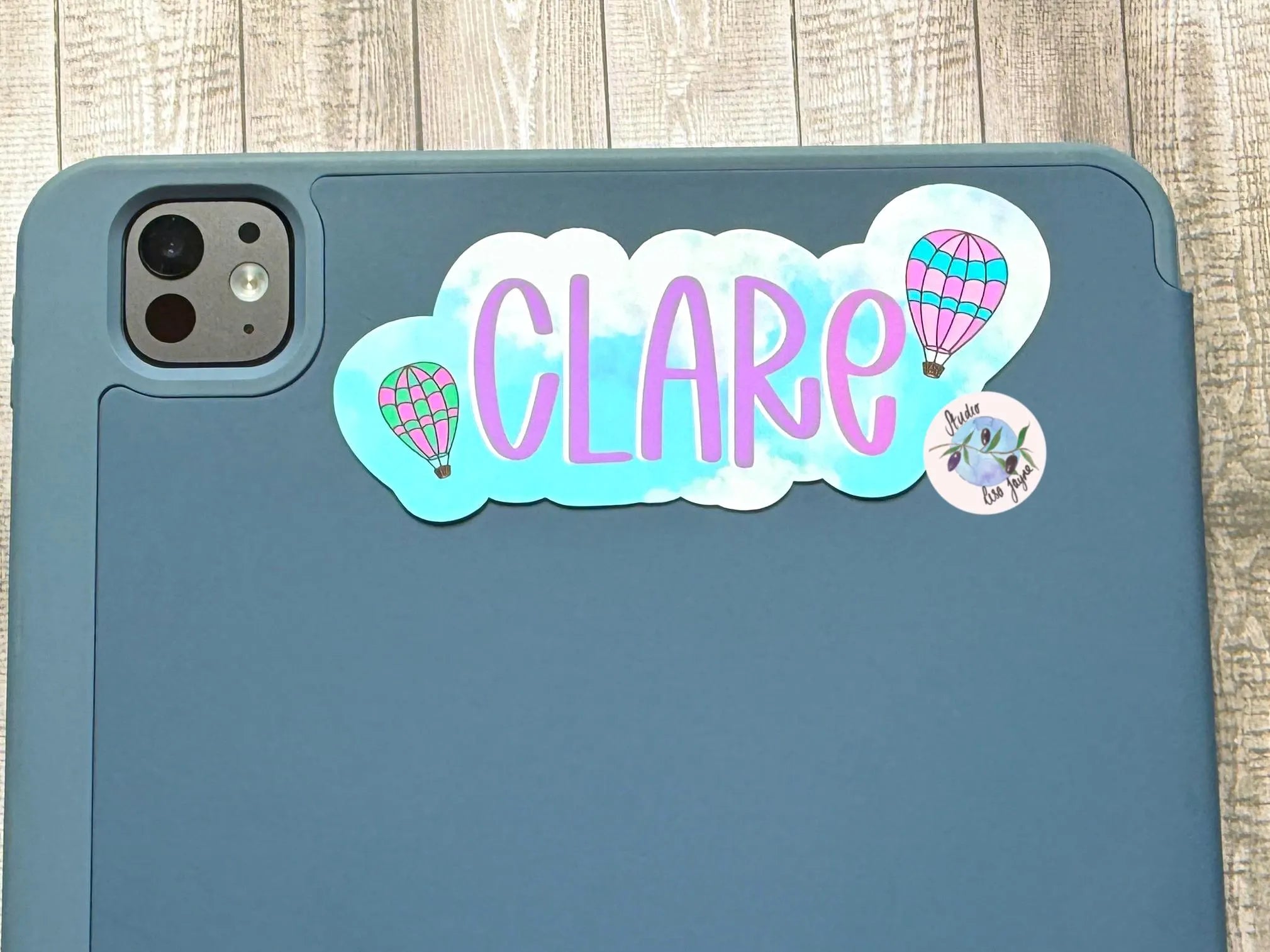 Phone case with 'CLARE' hot air baloon sticker on a wooden surface
