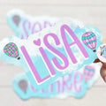 Personalized name sticker with 'Lisa' and hot air balloon designs on a light blue background.