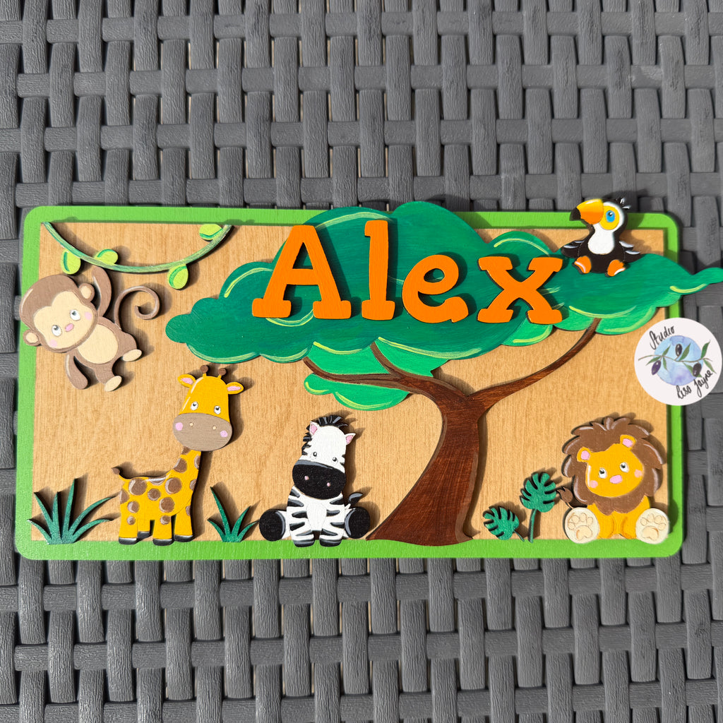 A personalized wooden name plaque featuring the name 'Alex' in orange letters under a green tree, surrounded by cartoon safari animals including a monkey, giraffe, zebra, lion, and penguin. The plaque is displayed on a gray woven mat background.