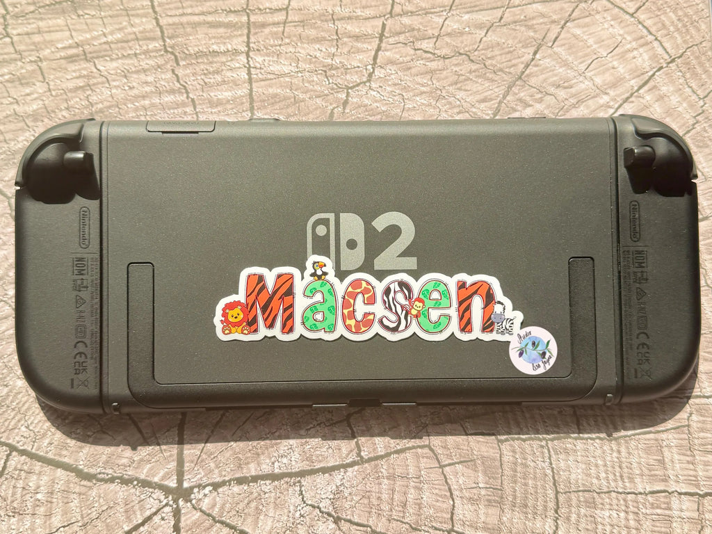 Black handheld device with colorful zoo themed name sticker.  Nintendo Switch 2